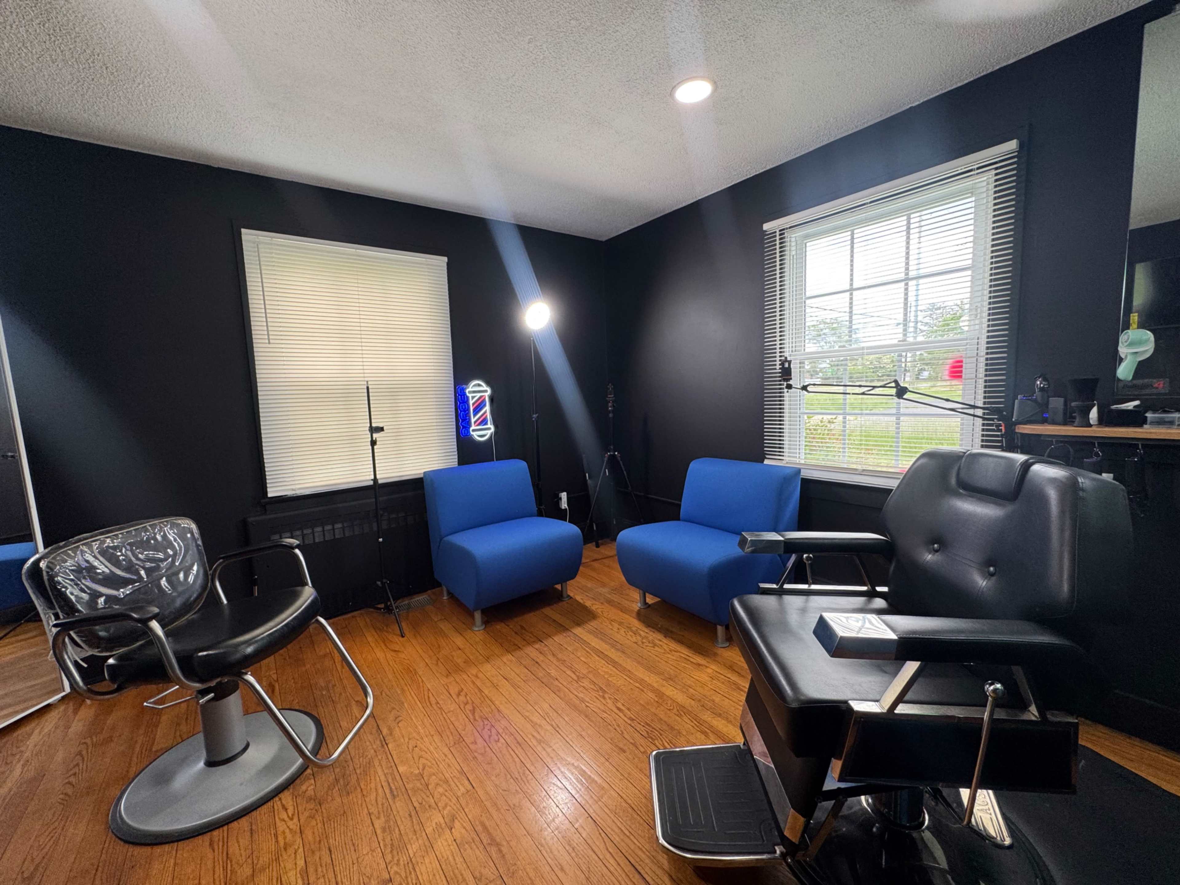 The image shows a barbershop interior with two blue chairs, a black barber chair, and a large window letting in natural light.