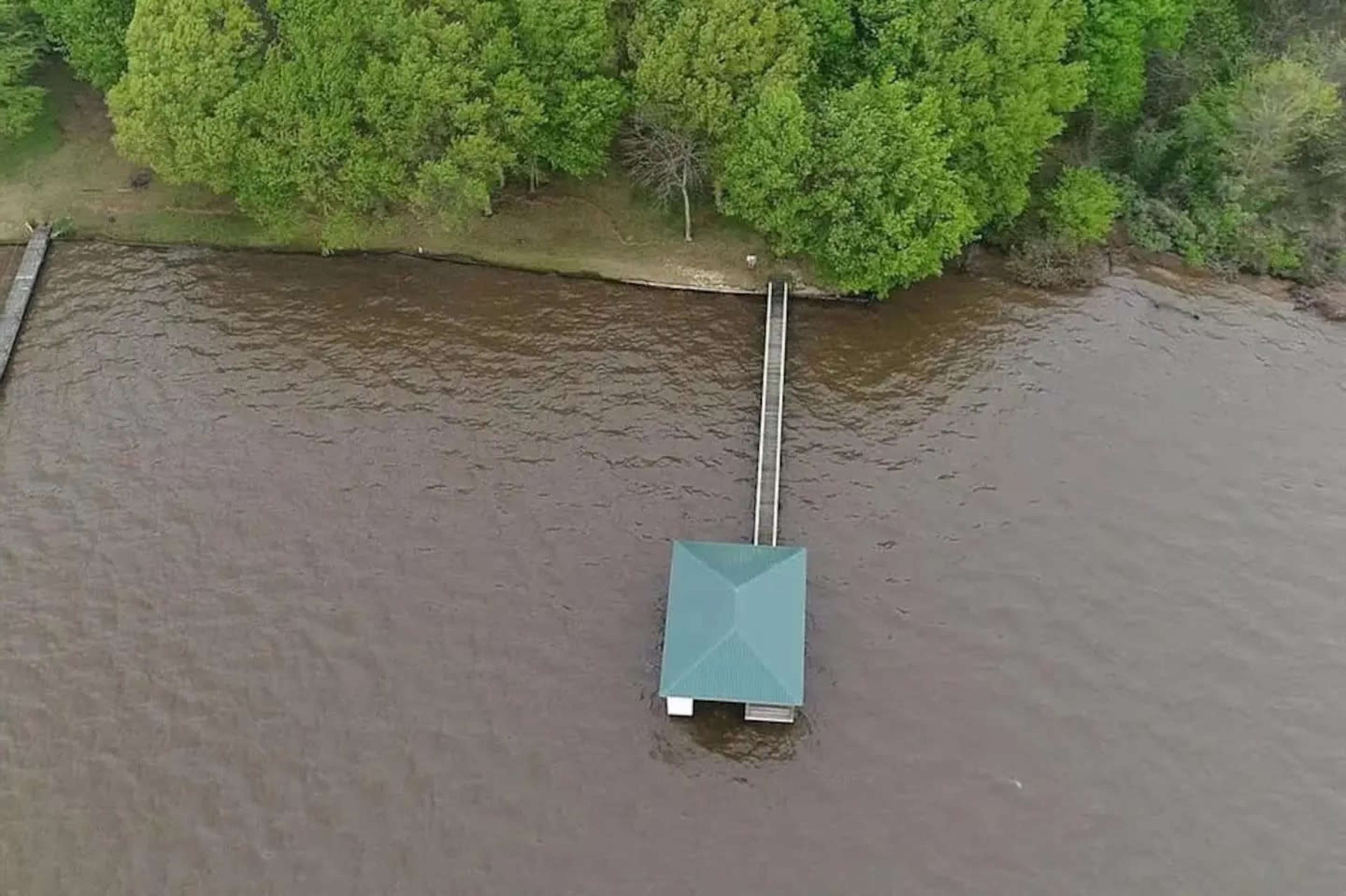 A small green-roofed dock extending over muddy water, surrounded by lush green trees.
