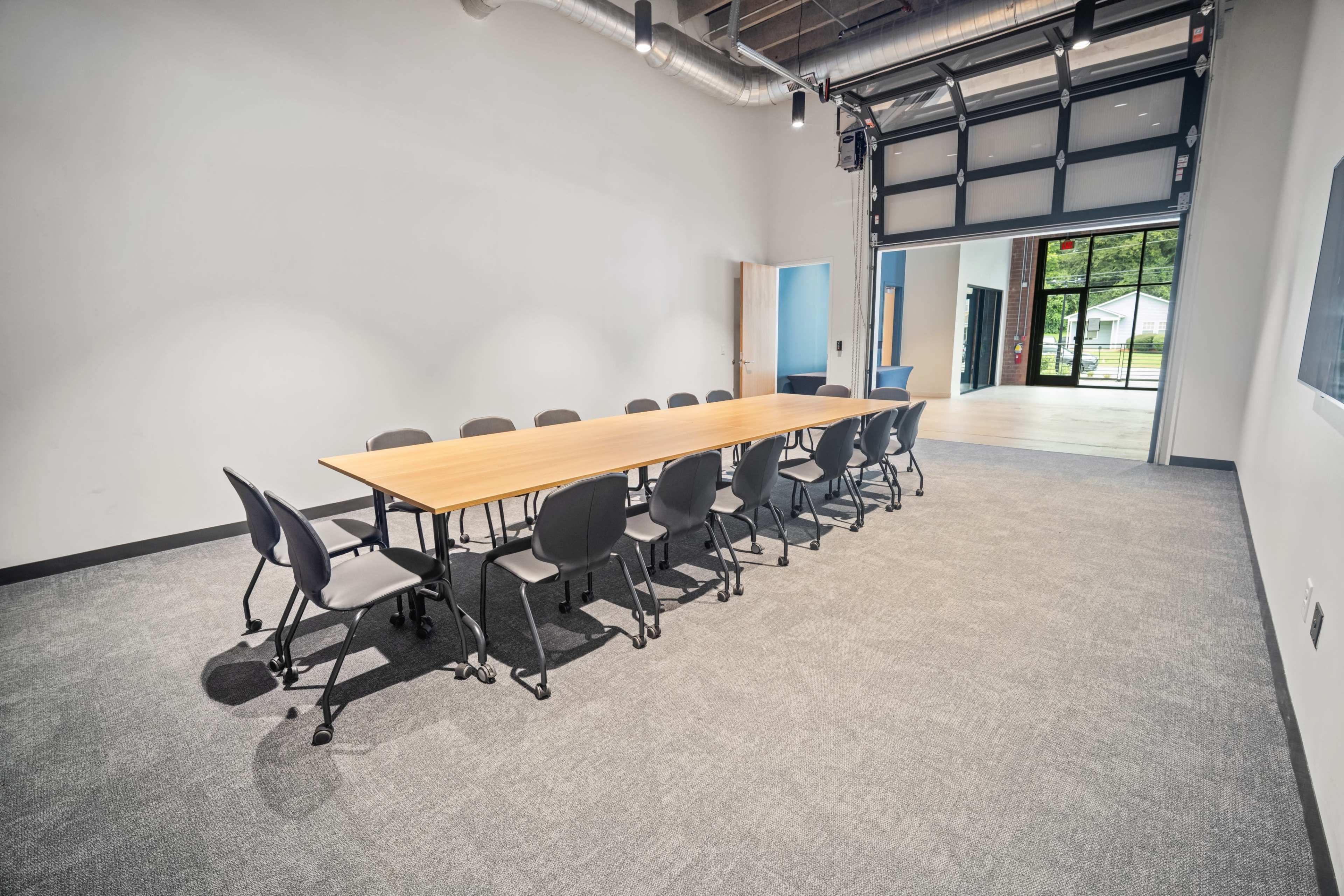 A long wooden table is arranged with ten black chairs on each side in a spacious, empty conference room.