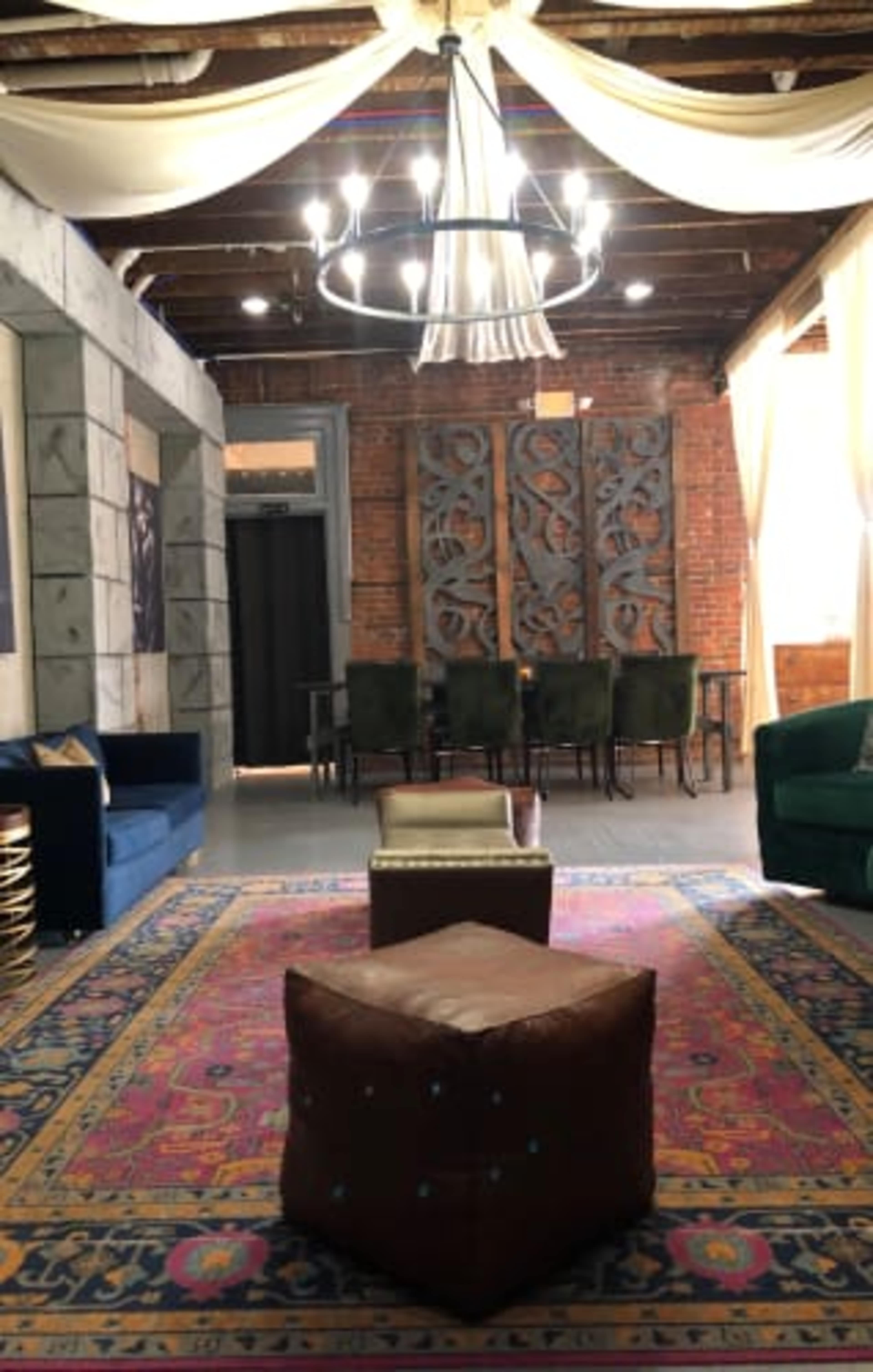 A spacious room with rustic brick walls, a patterned area rug, two couches, a chandelier, and decorative panels.