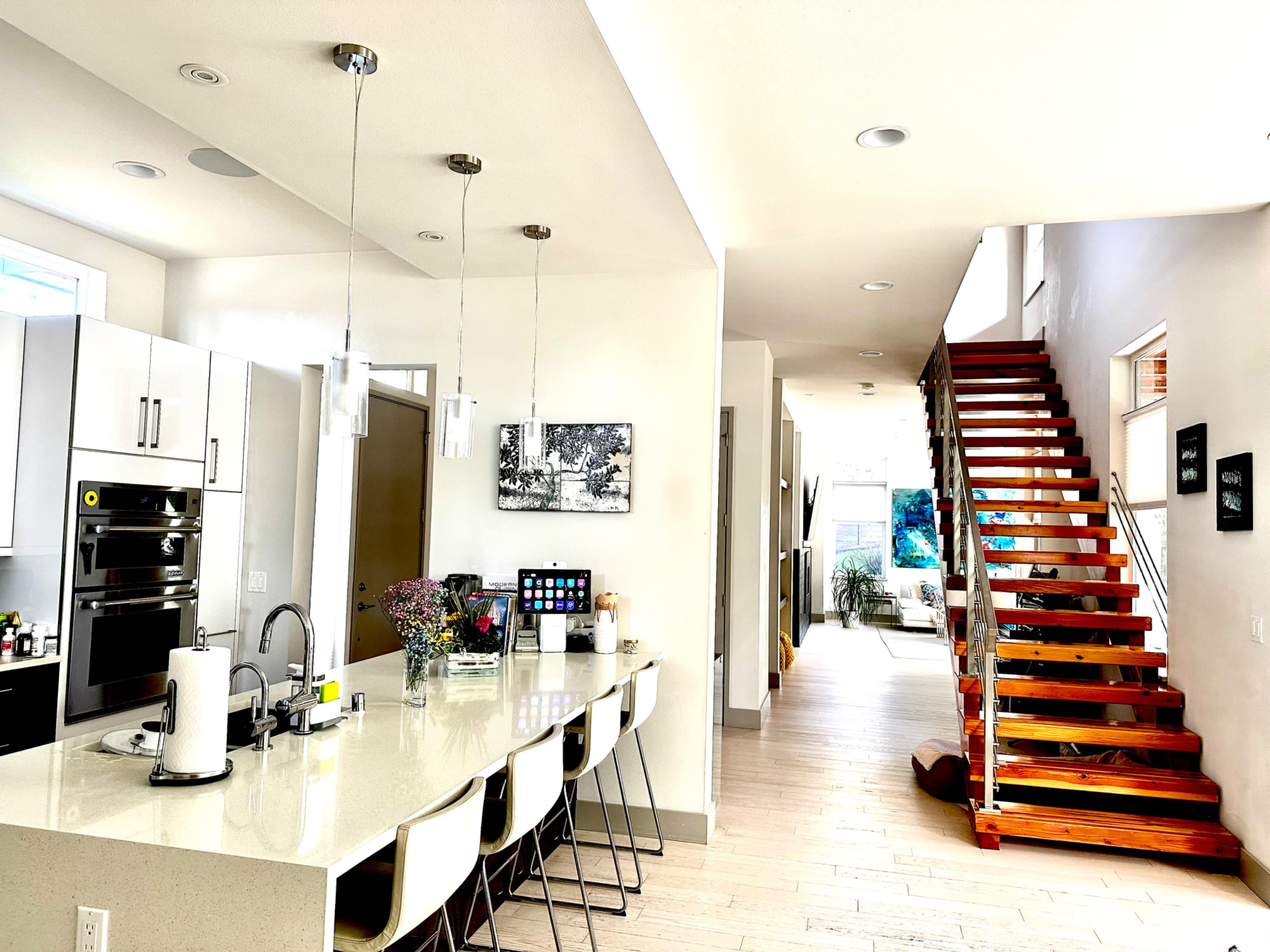 A modern kitchen with white cabinets and a large island, leading to a staircase made of wooden steps.