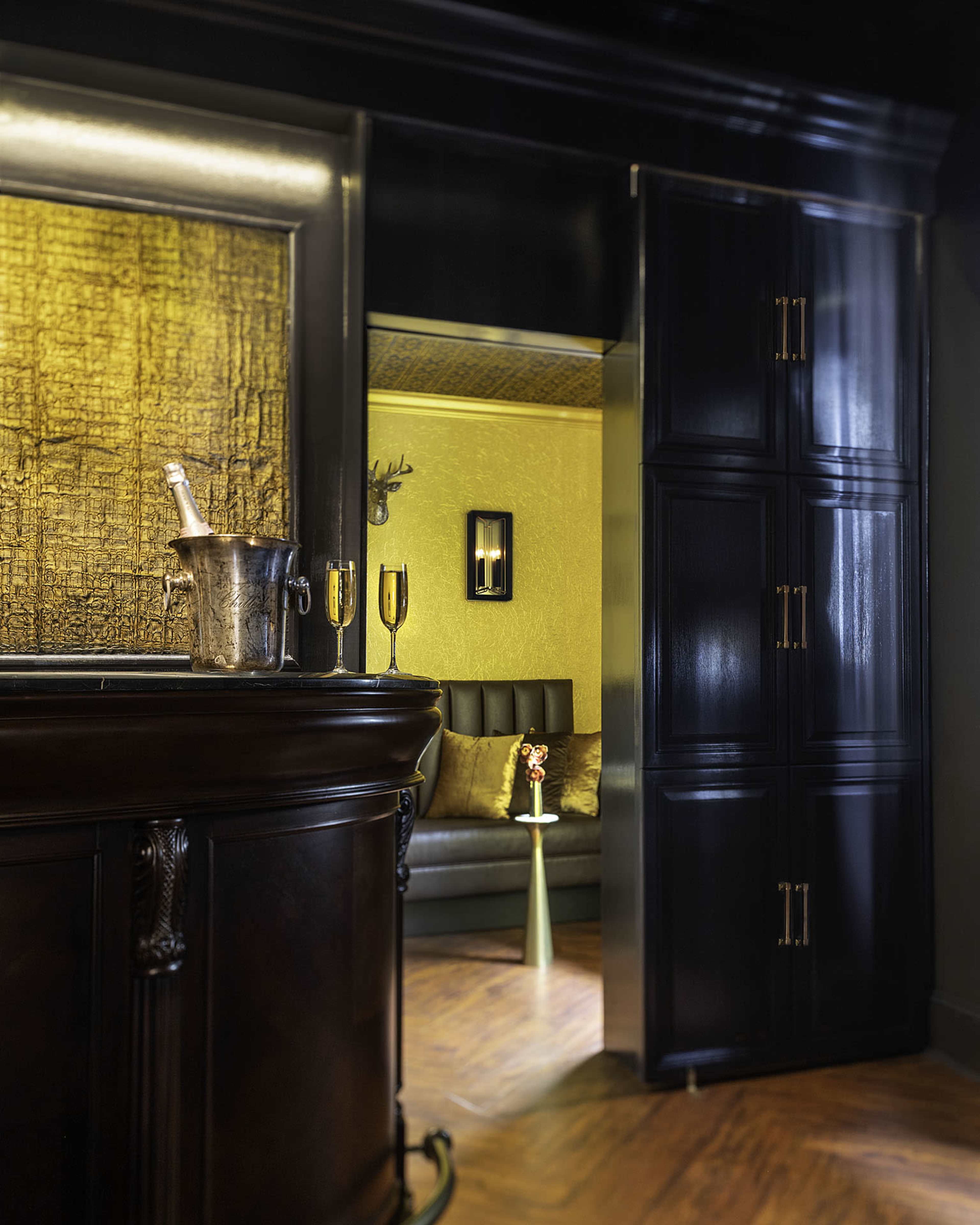 A dark, elegant bar area leads to a cozy room with a greenish-yellow wall and a gray sofa.