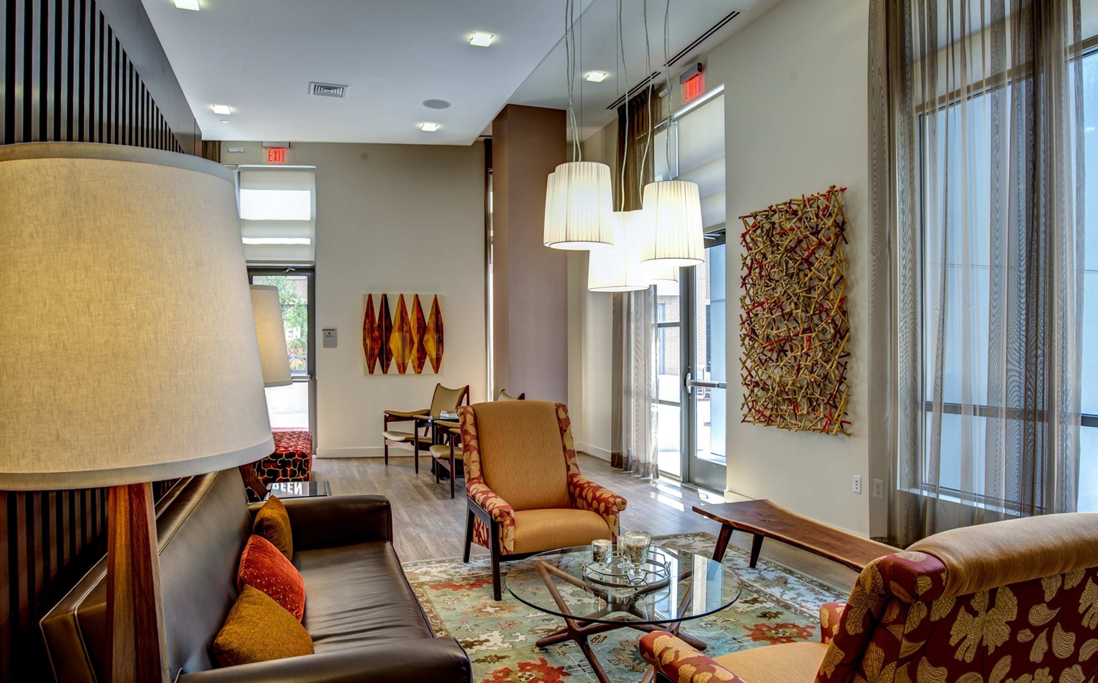A modern lounge area with two armchairs, a sofa, a coffee table, and decorative wall art, illuminated by pendant lights.