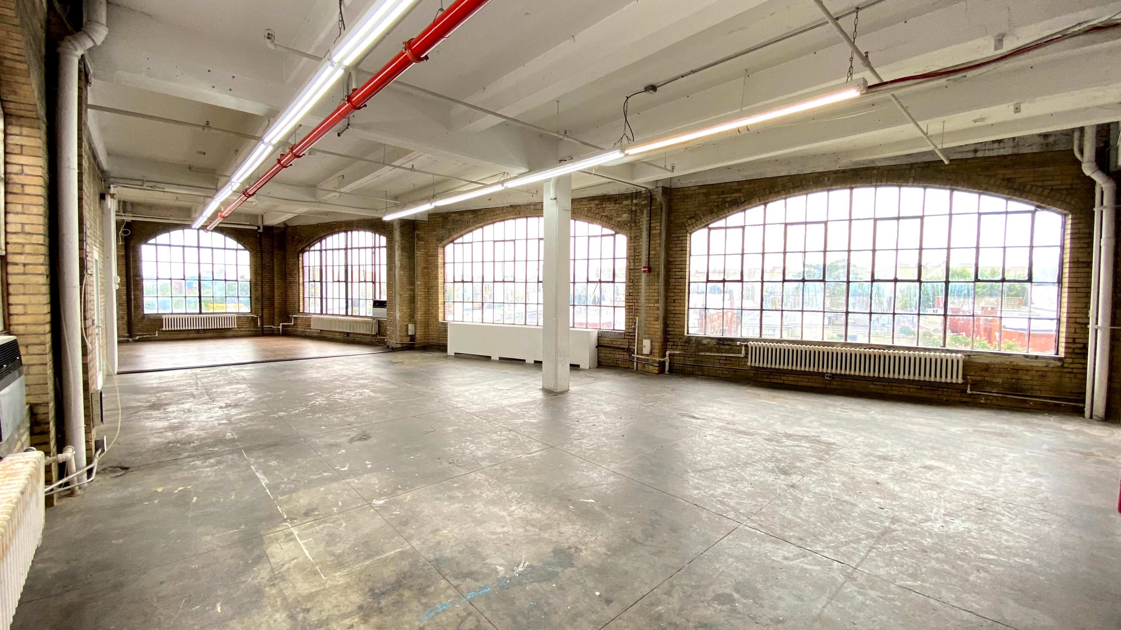 An empty industrial-style room with large arched windows and a concrete floor.