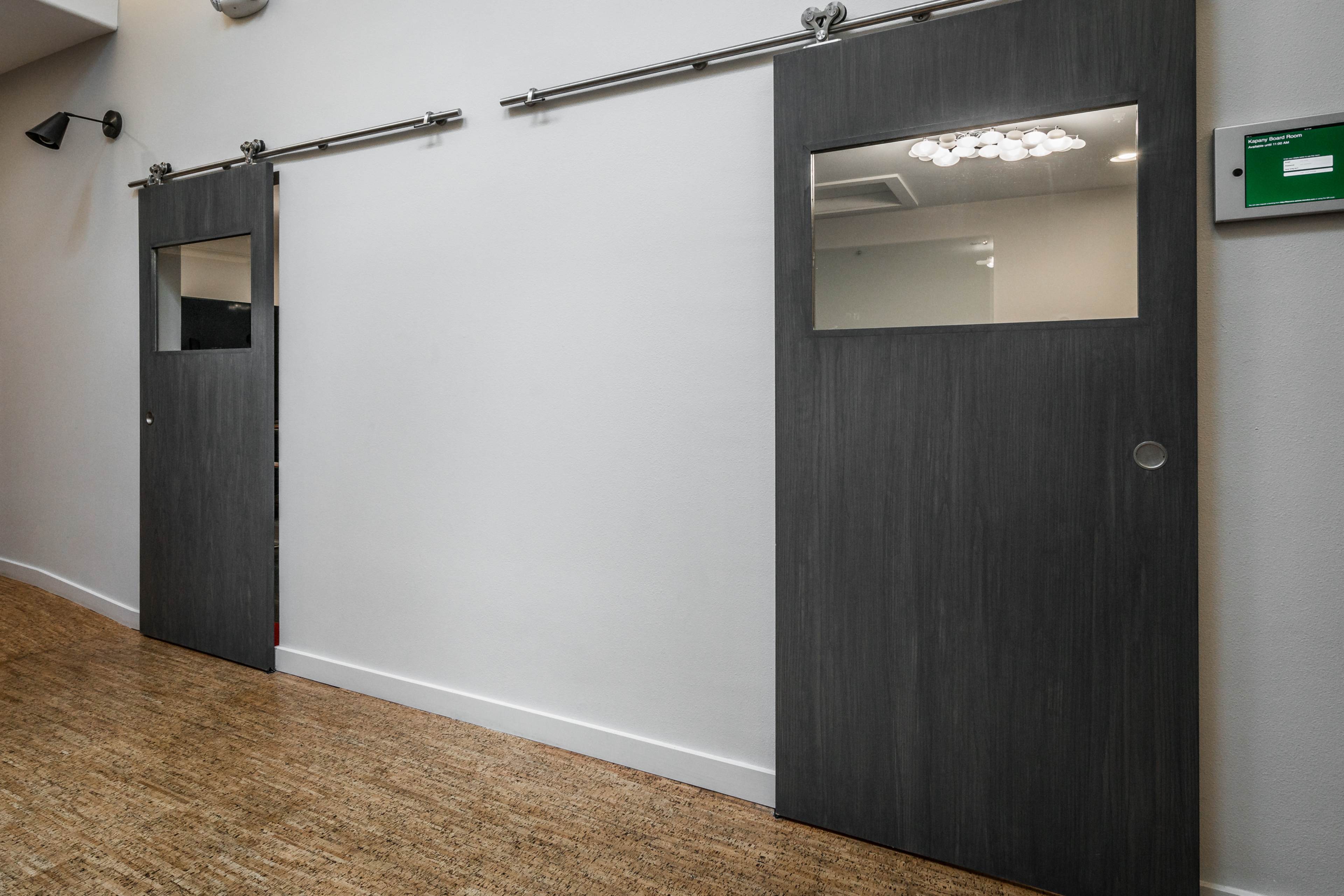 Two sliding doors mounted on a track in a simple interior corridor.
