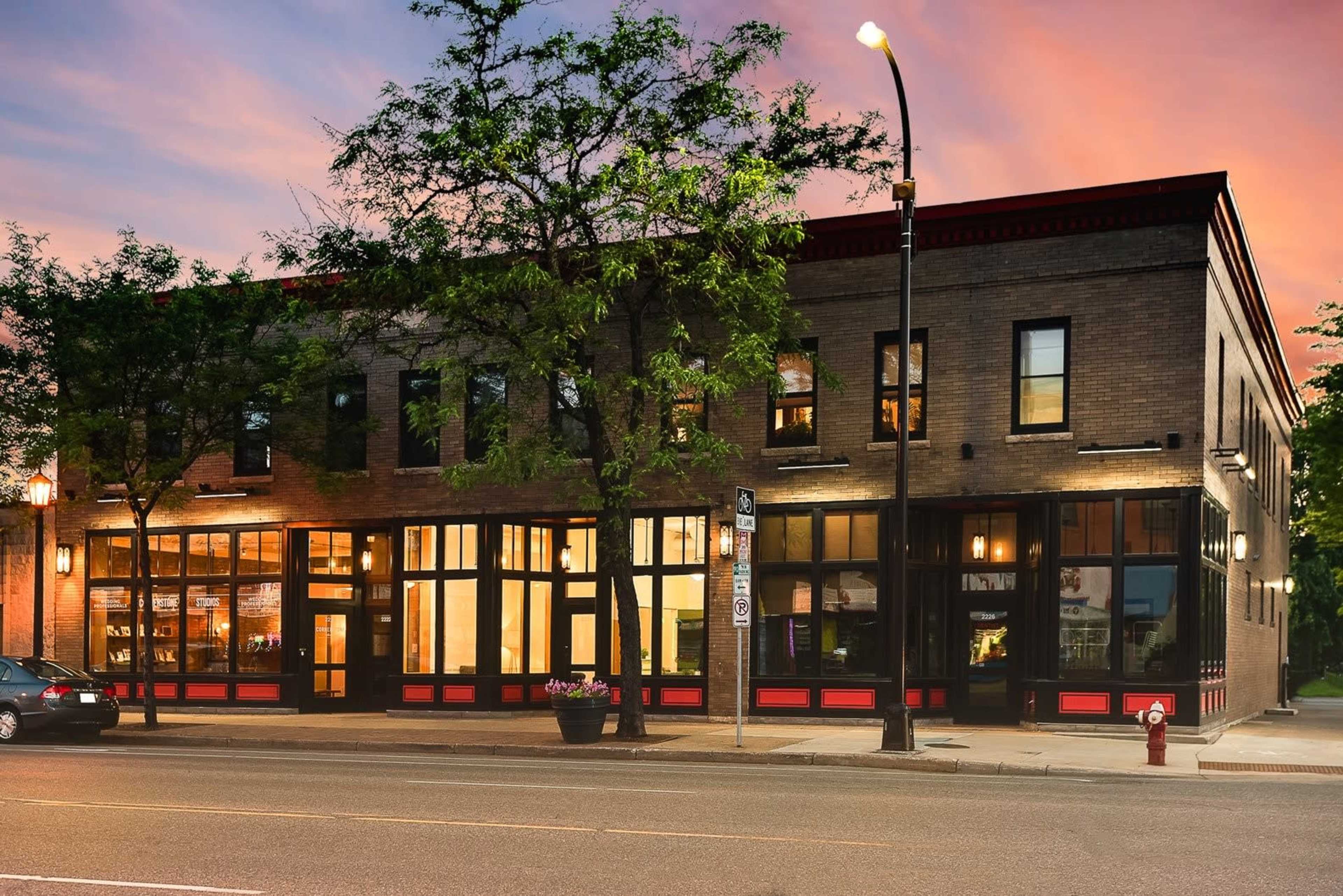 A two-story brick building with large windows, located on a city street at dusk, featuring a red and black color scheme.