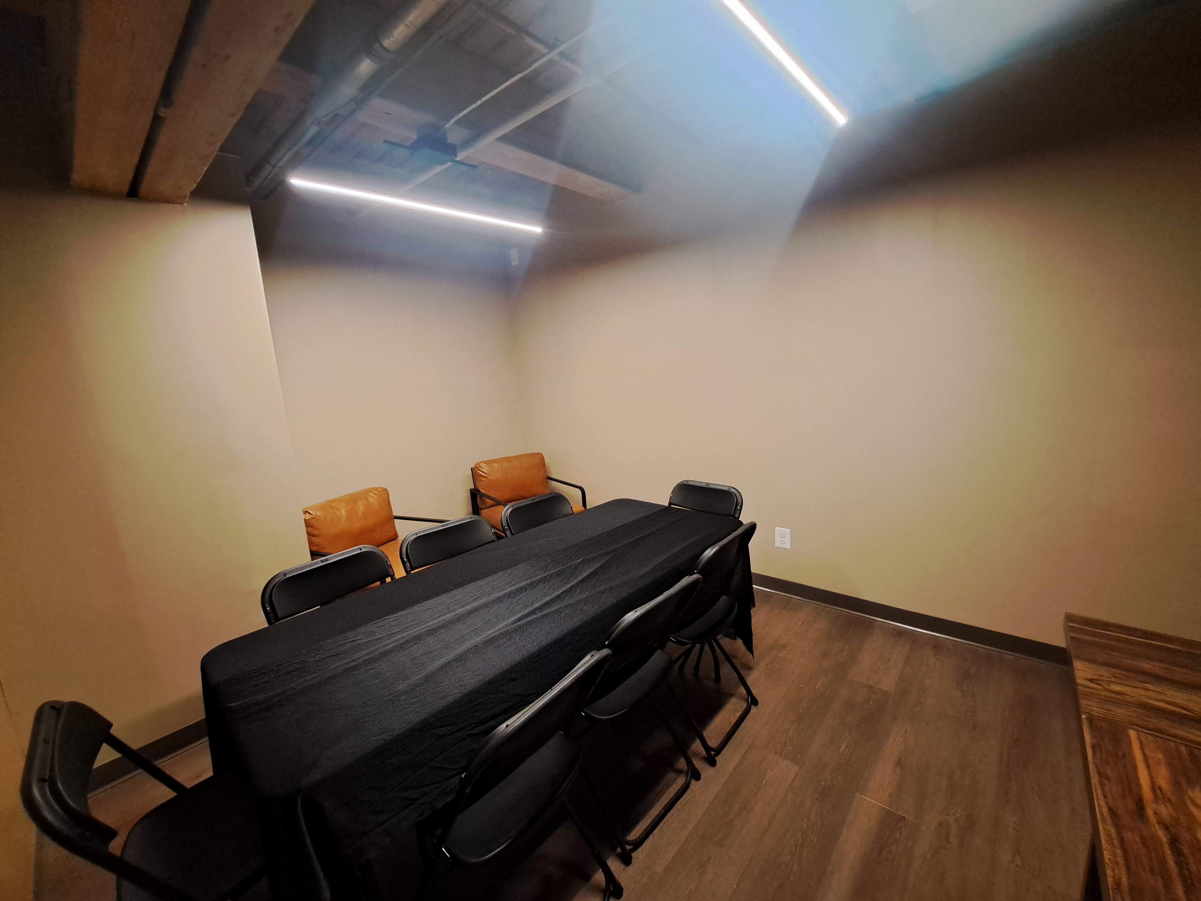 A small meeting room features a long black table surrounded by folding chairs and two leather armchairs in a corner.