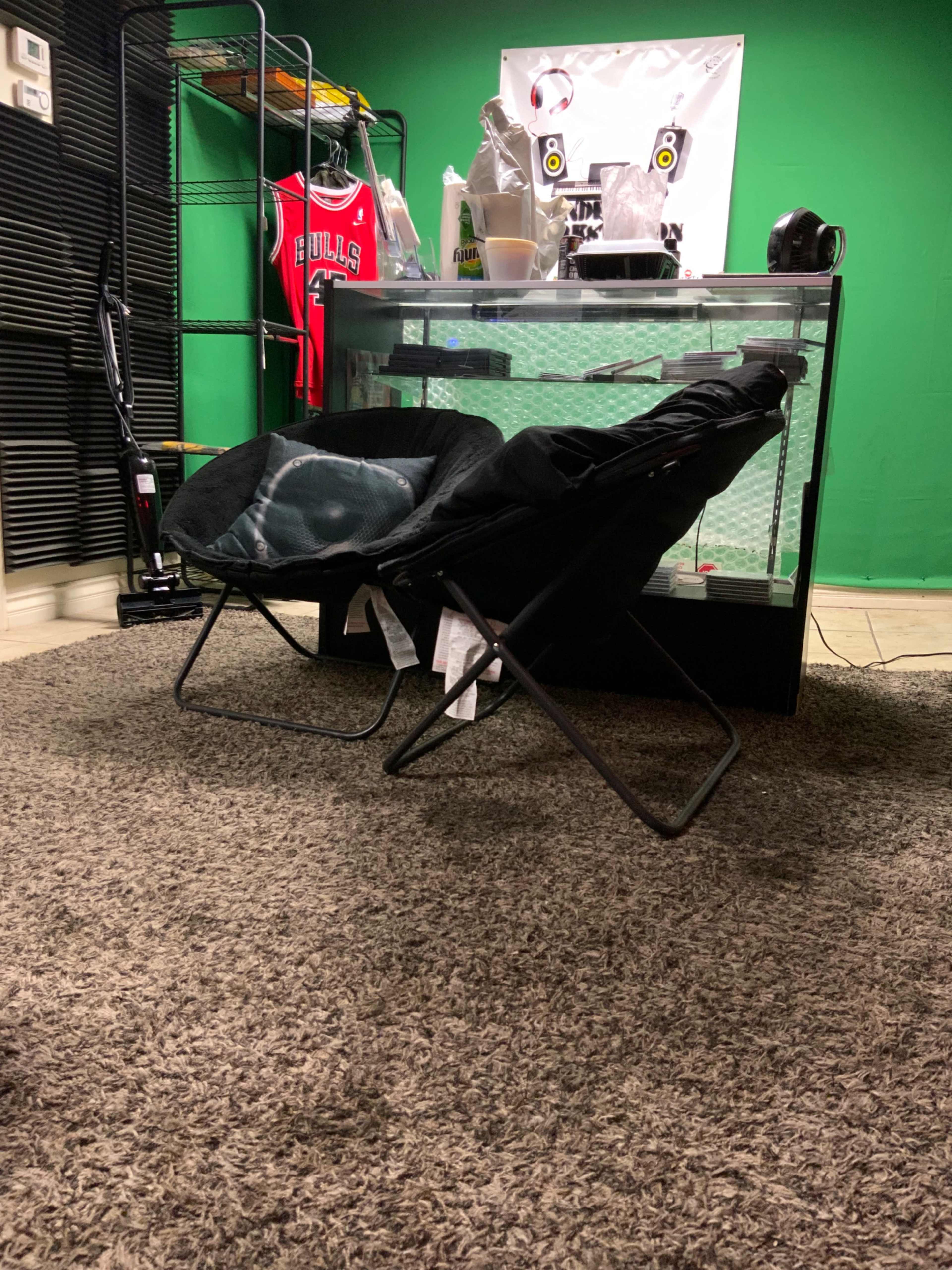 Two folding chairs placed on a carpeted floor in a room with a green backdrop and a display table.