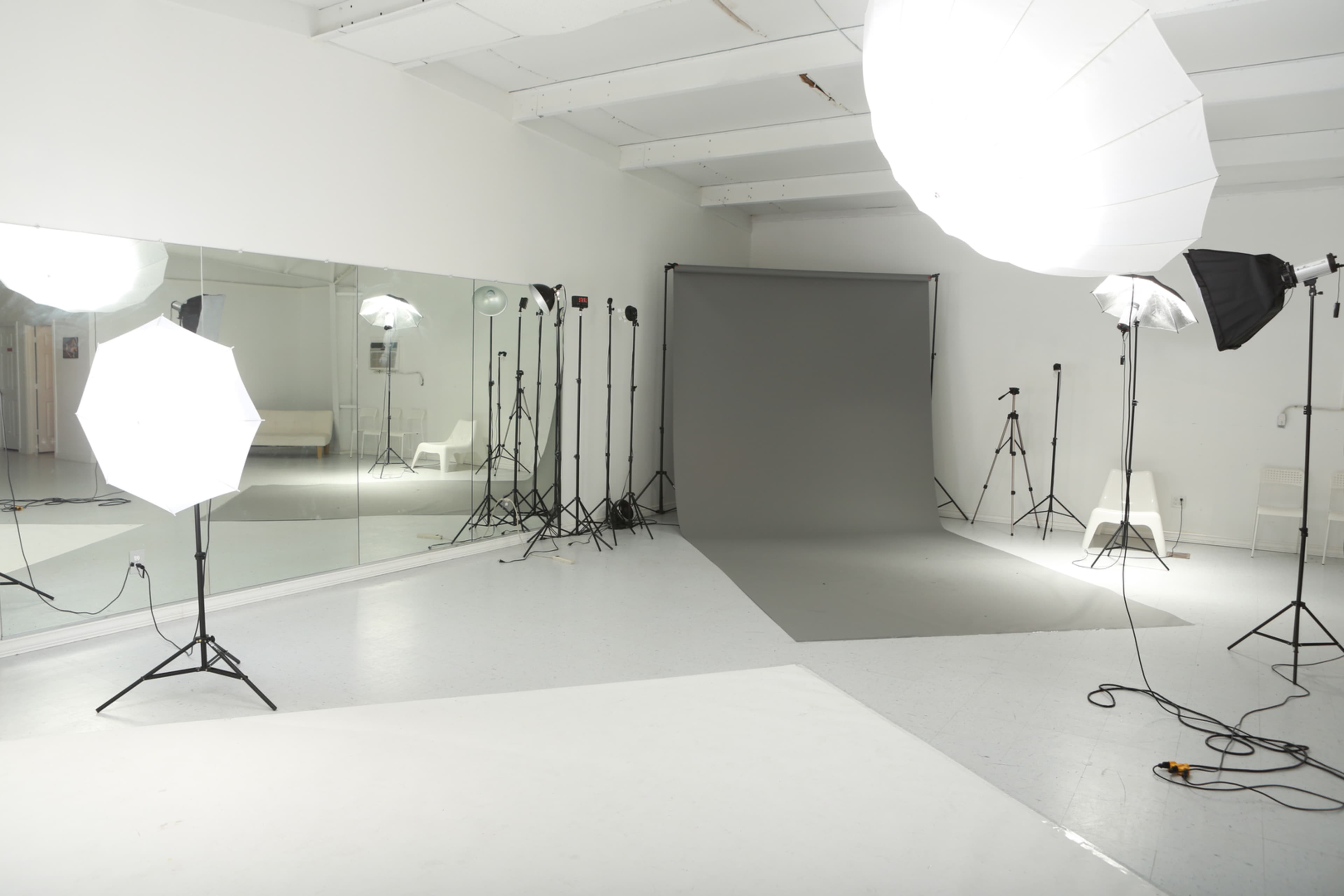 A photography studio equipped with multiple softbox lights, a large mirror, and a gray backdrop.