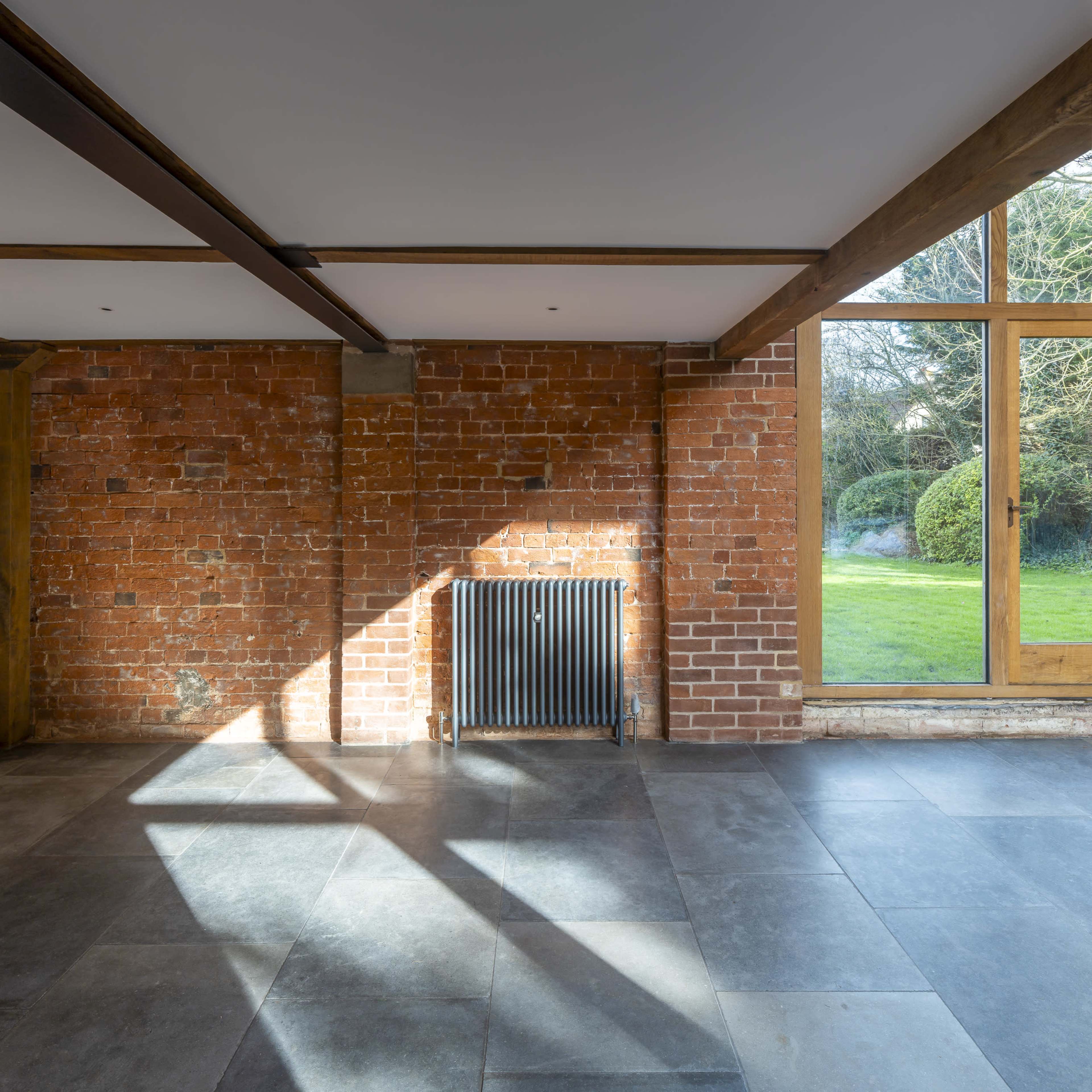 The interior of a room features a vintage radiator against a brick wall, with a large window overlooking a grassy yard.