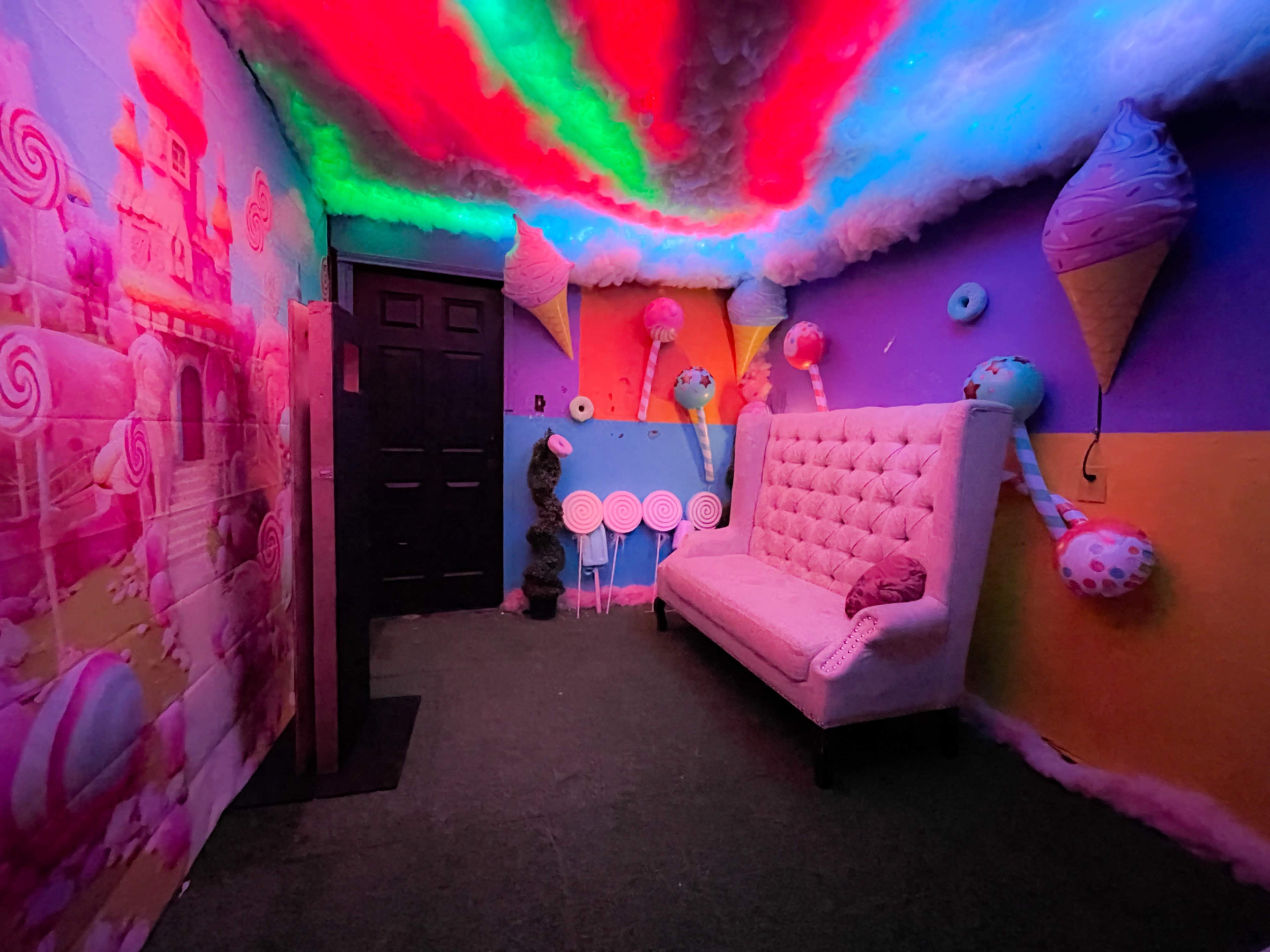 The room features colorful walls decorated with candy-themed decorations, including oversized ice cream cones and lollipops, along with a plush white sofa.