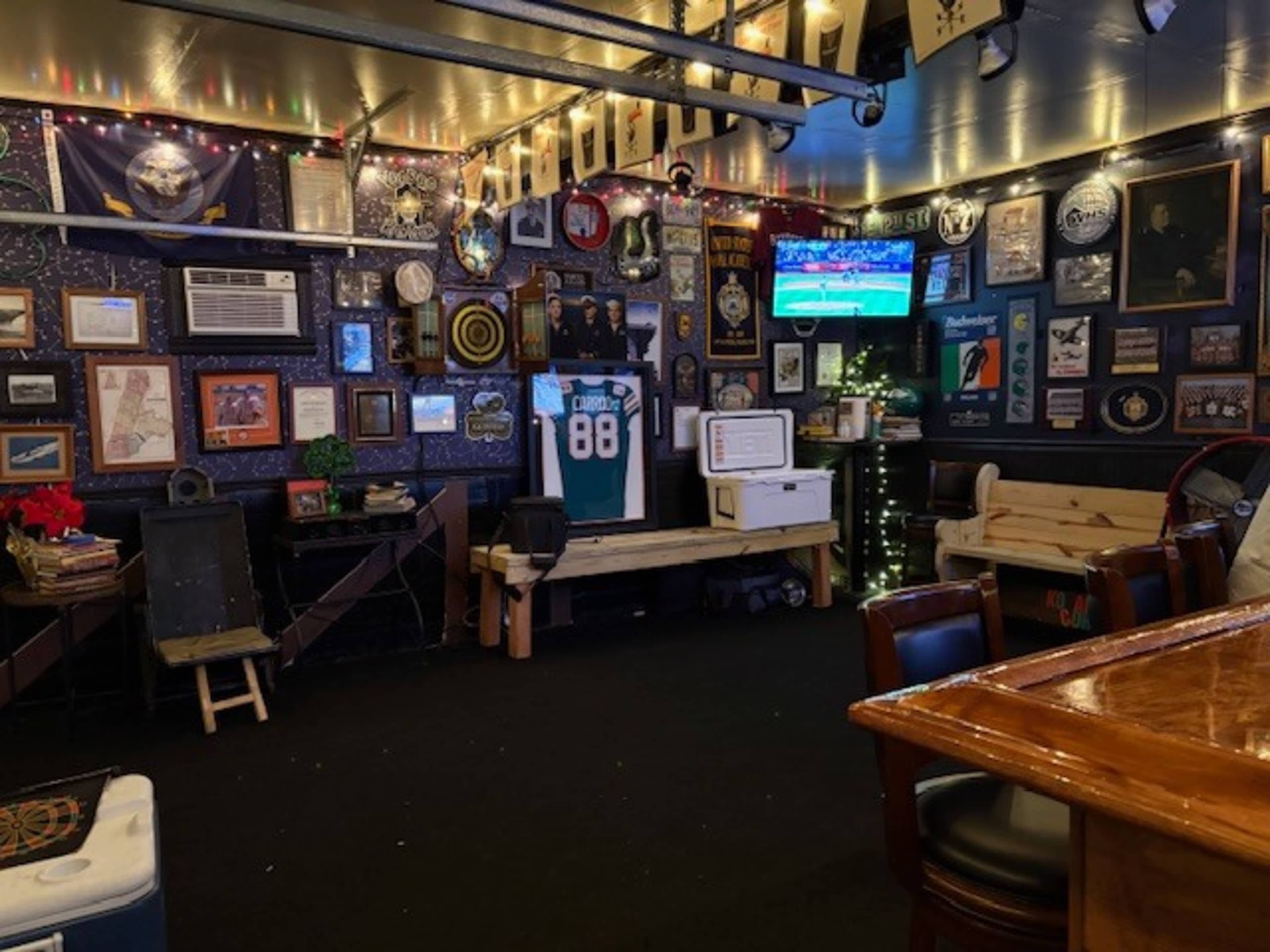 The image shows the interior of a sports-themed bar, featuring memorabilia, a television showing a game, and wooden benches against the walls.