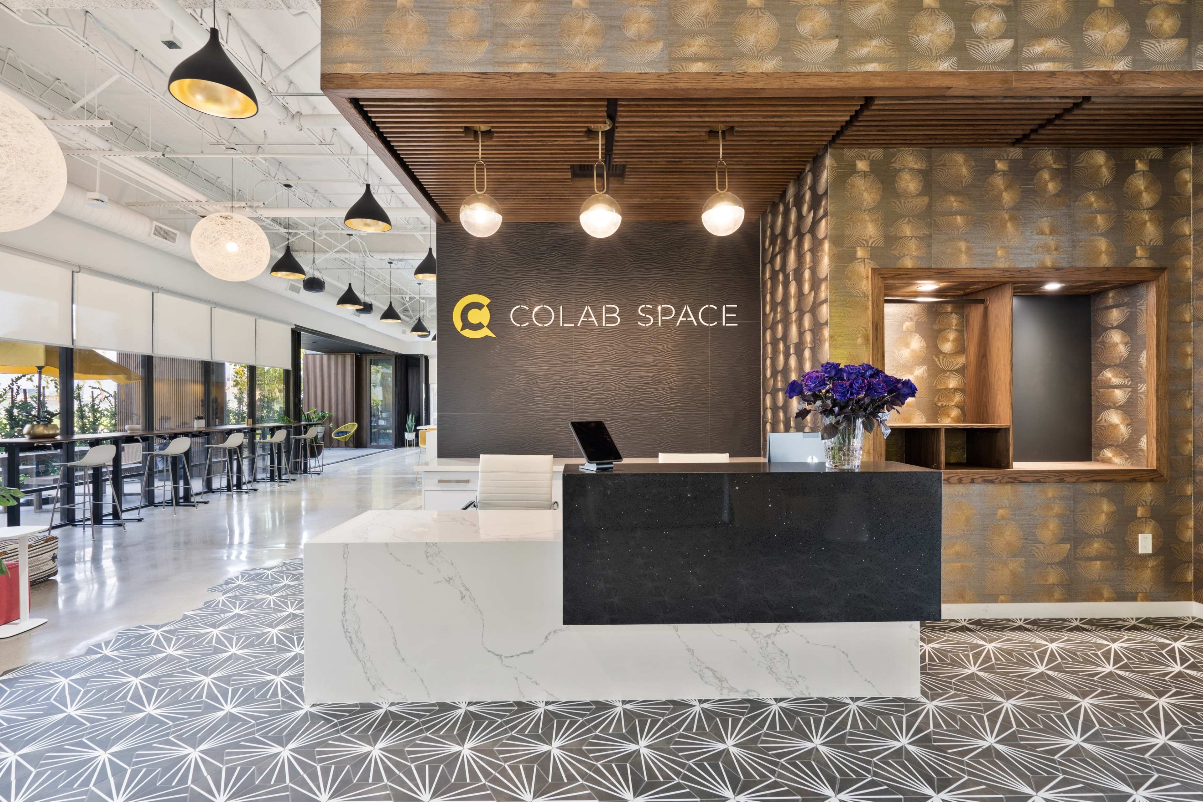 The image shows a modern reception area labeled "COLAB SPACE," featuring a sleek front desk with a dark counter, decorative wall patterns, and seating in the background.