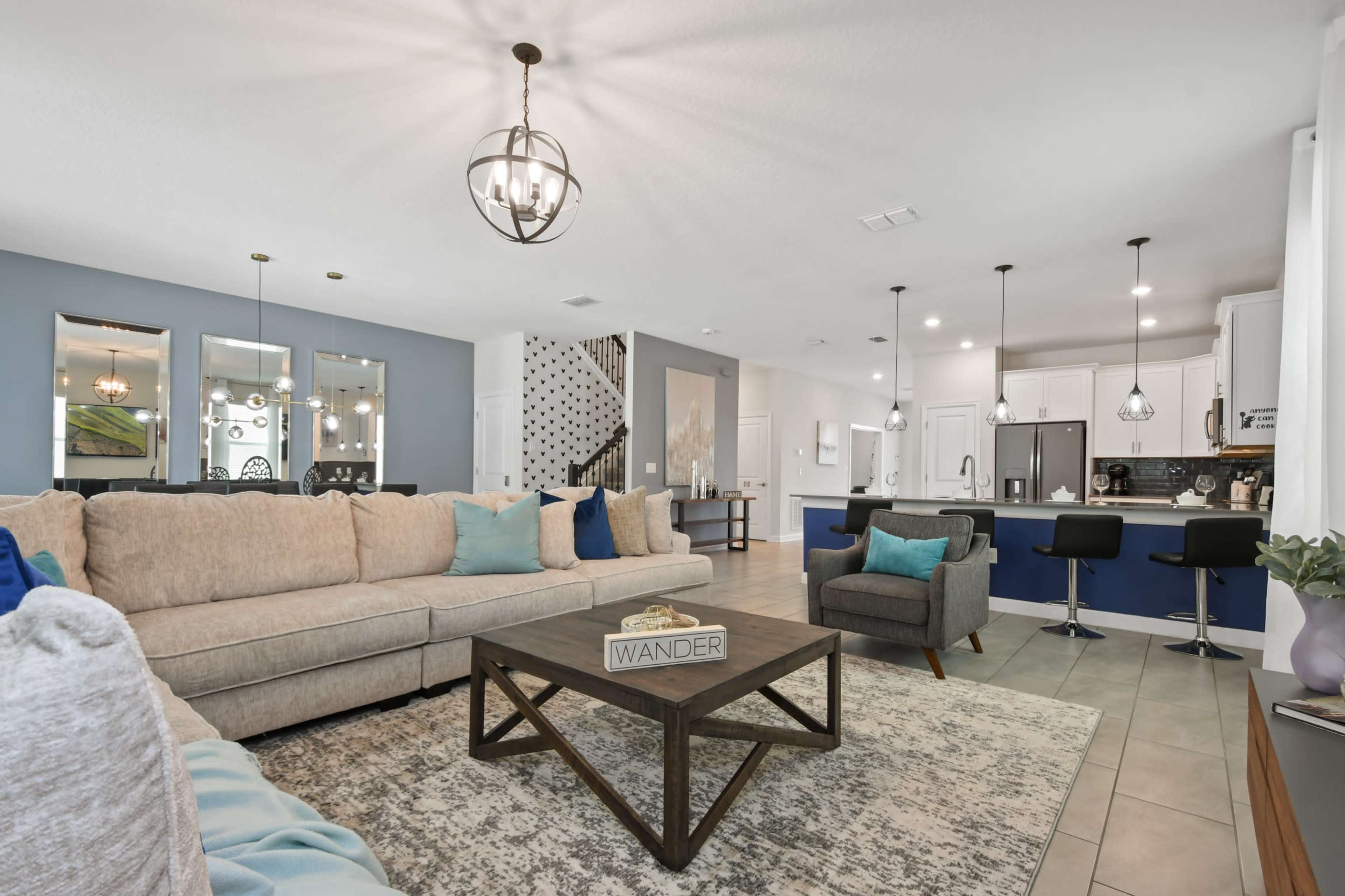 A modern living room with a large sectional sofa, a coffee table, and an open kitchen area with pendant lights and bar seating.