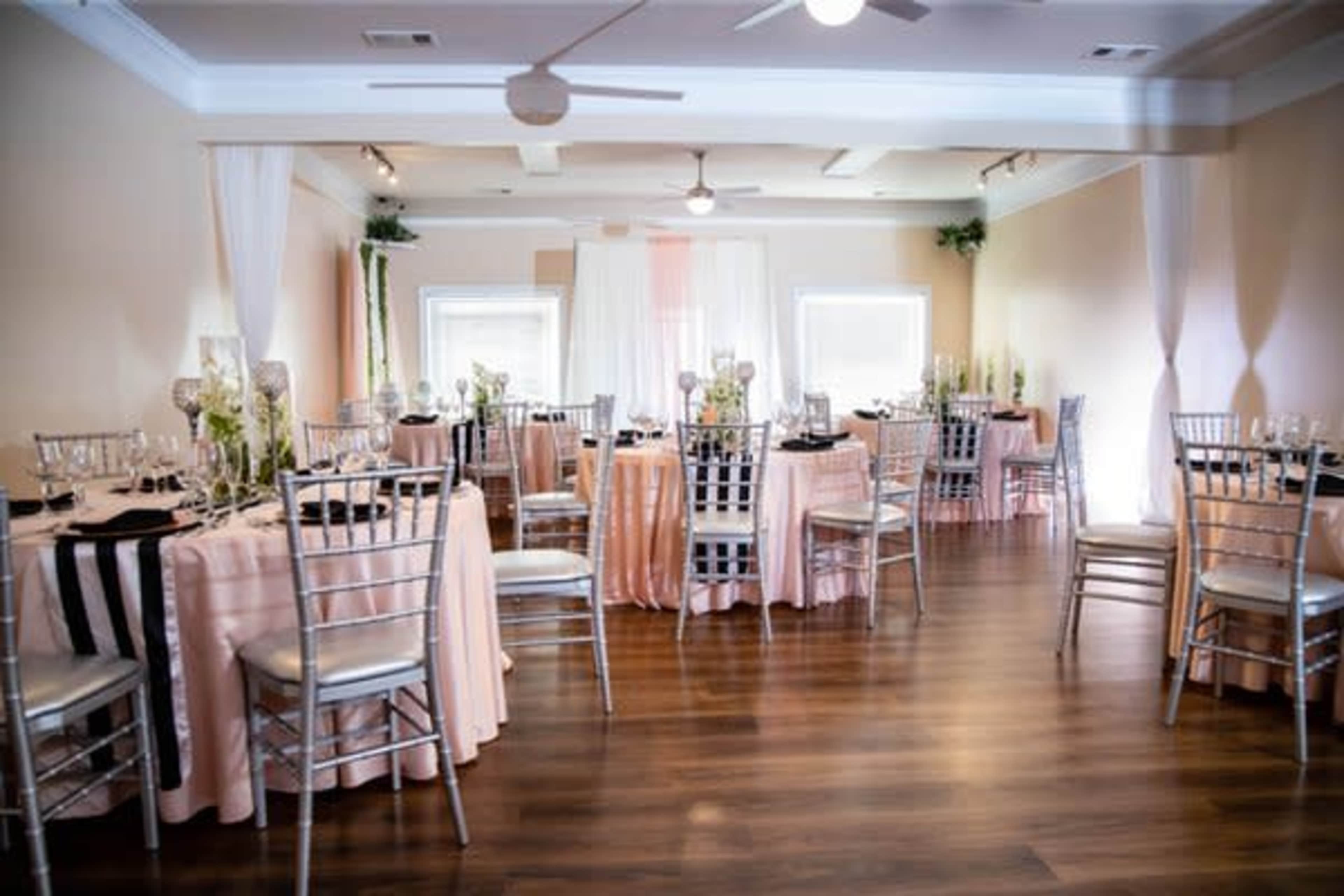 A banquet room set with round tables covered in pink and black tablecloths, elegant place settings, and decorative centerpieces.