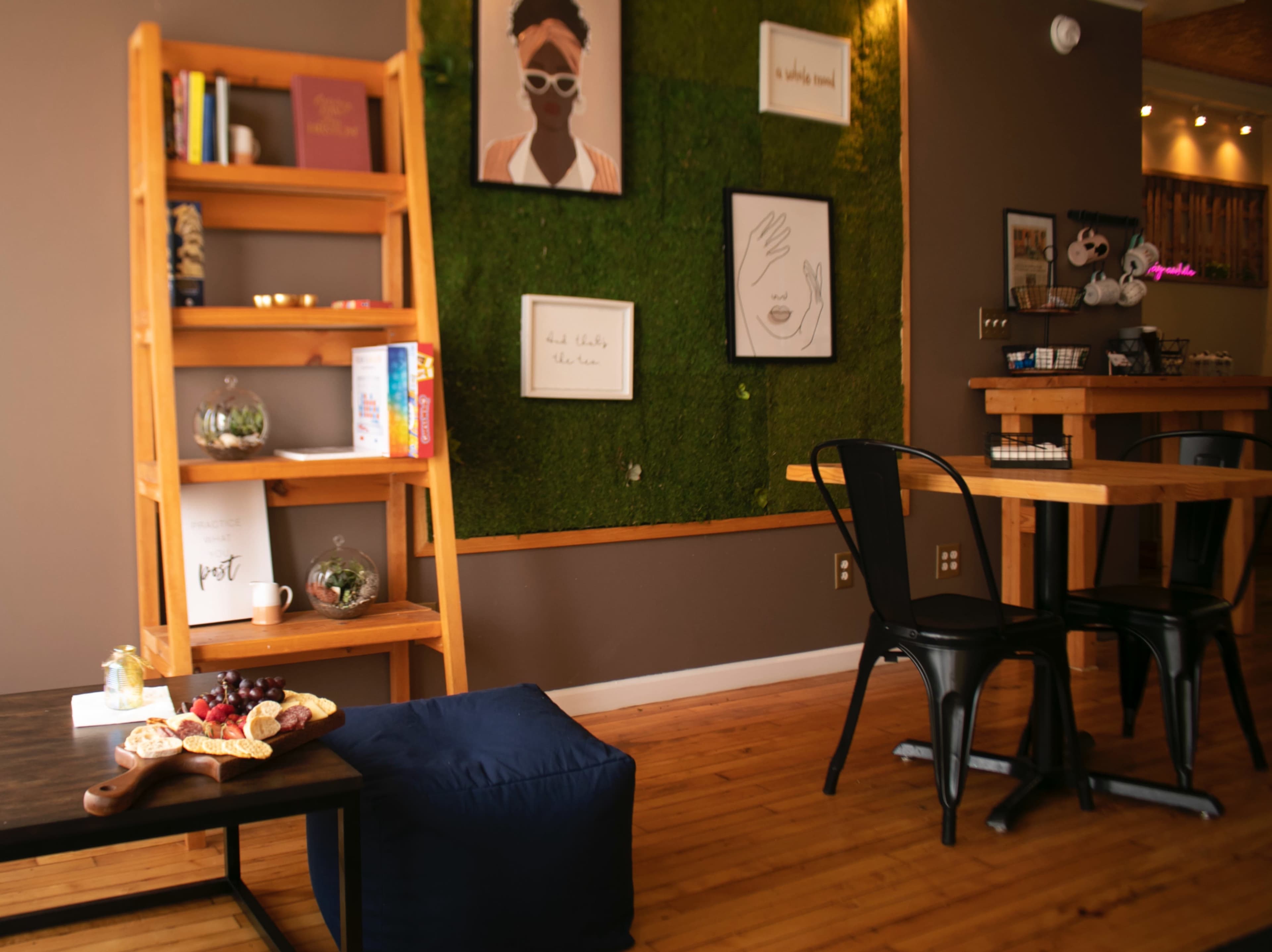 A cozy interior with wooden furniture, a green moss wall, shelves with books and decorations, and a small table set with snacks.