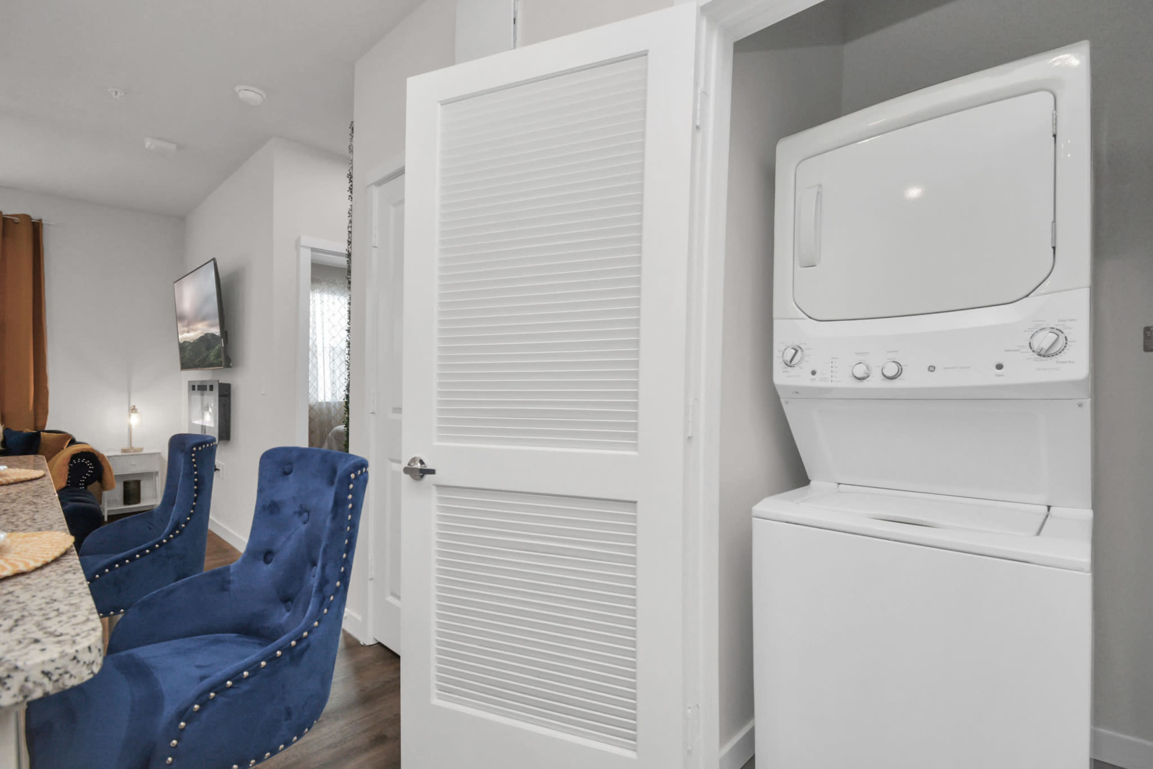 The image shows a compact laundry area featuring a stacked washer and dryer next to a partially open door in a modern apartment.