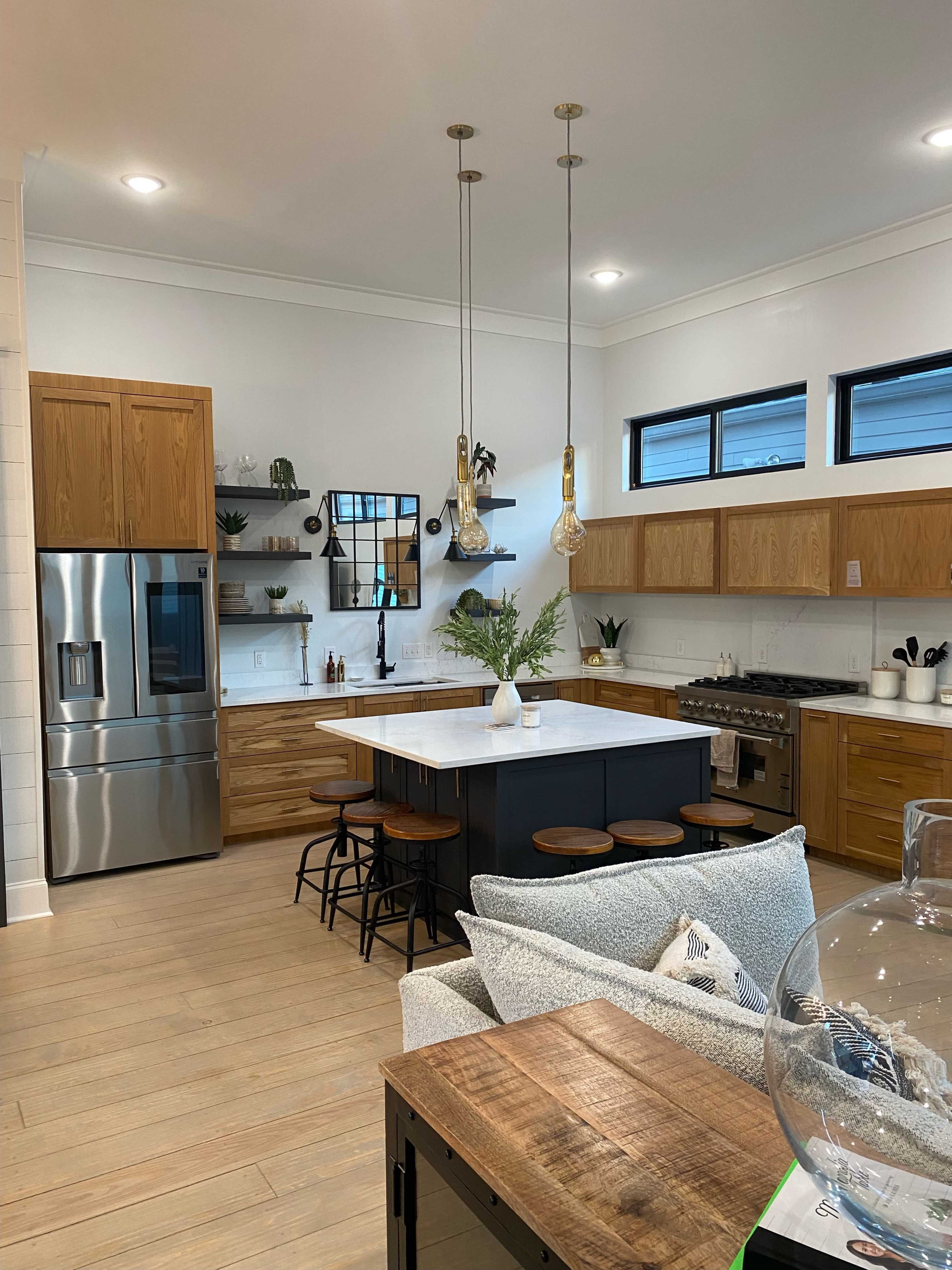 A modern kitchen with wooden cabinets, a large island with seating, and pendant lights overhead.