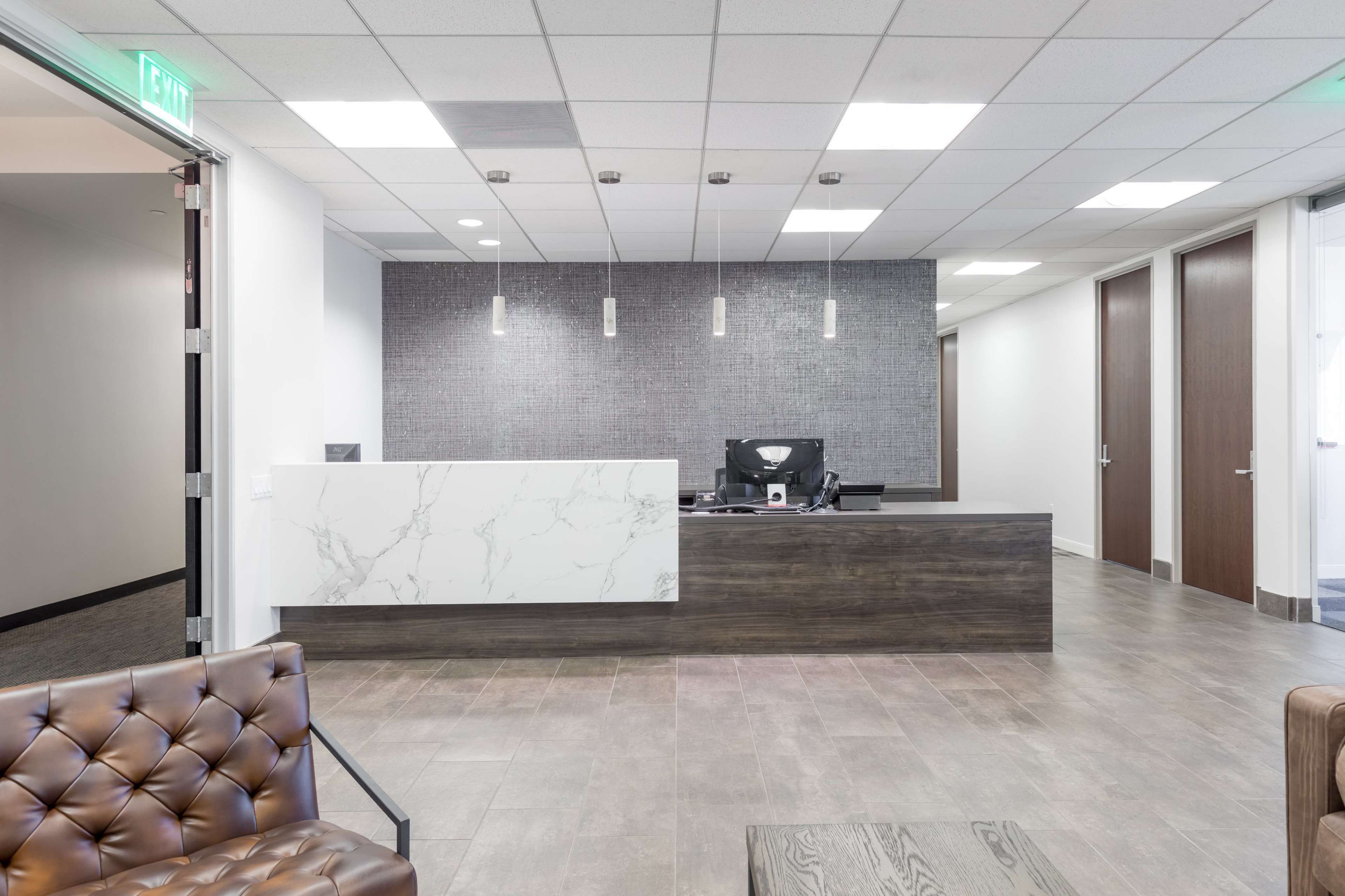 A modern reception area featuring a desk with a marble front, a computer setup, and a seating area with a brown leather chair.