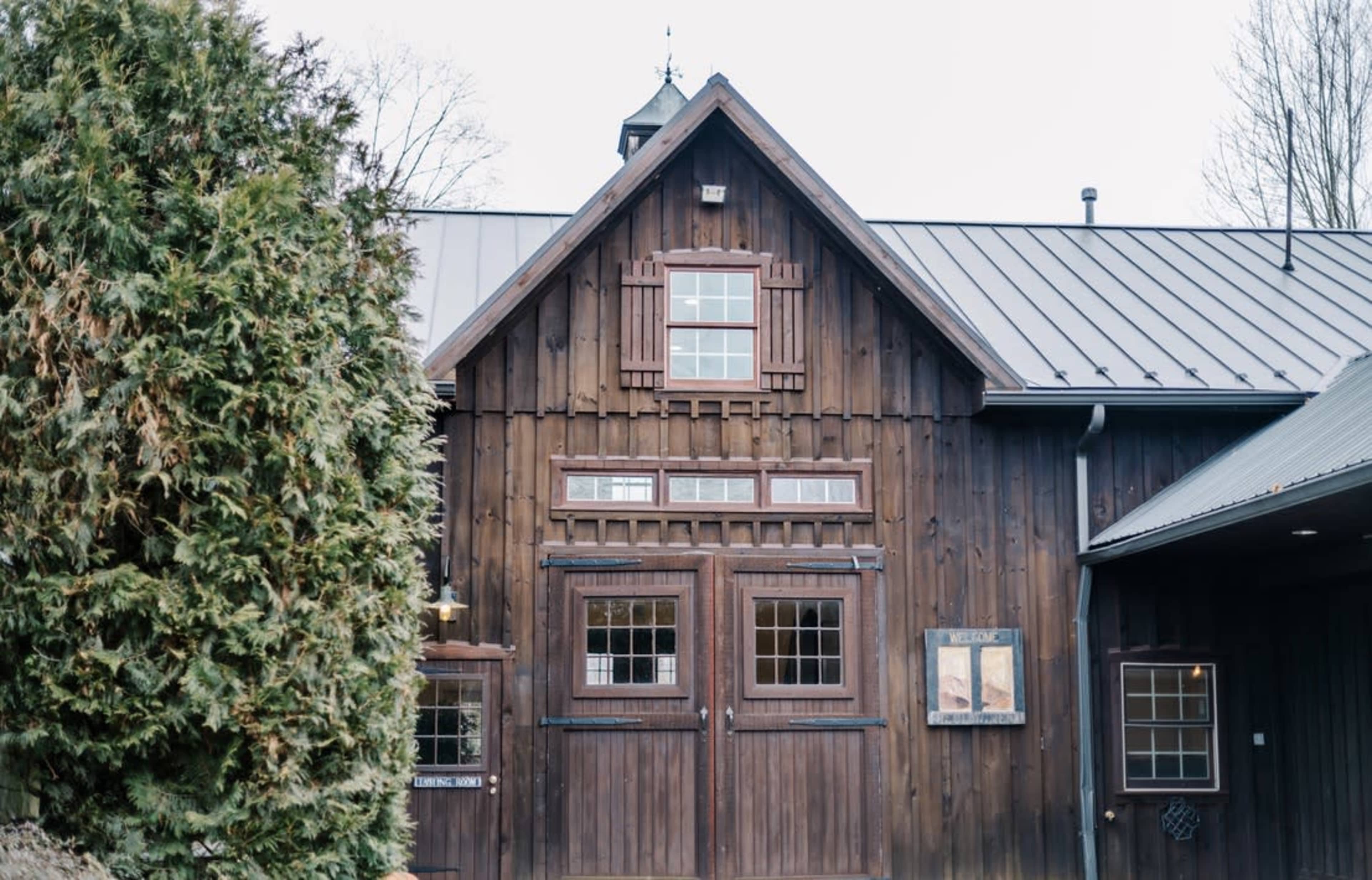 The image shows a rustic wooden barn with large double doors and several windows.