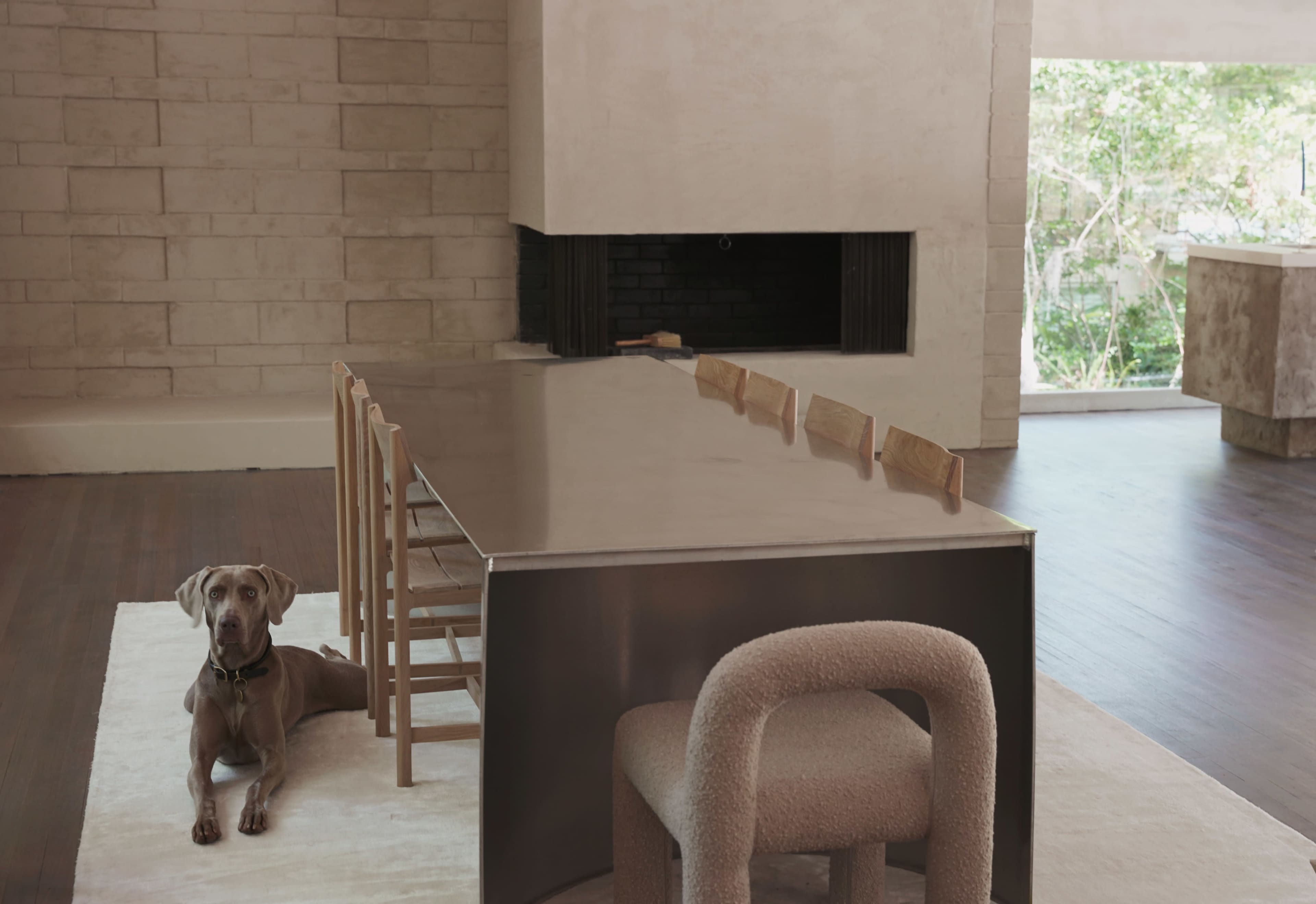 A sleek, metallic dining table is positioned in a spacious room, accompanied by a dog resting on a rug beside the table.
