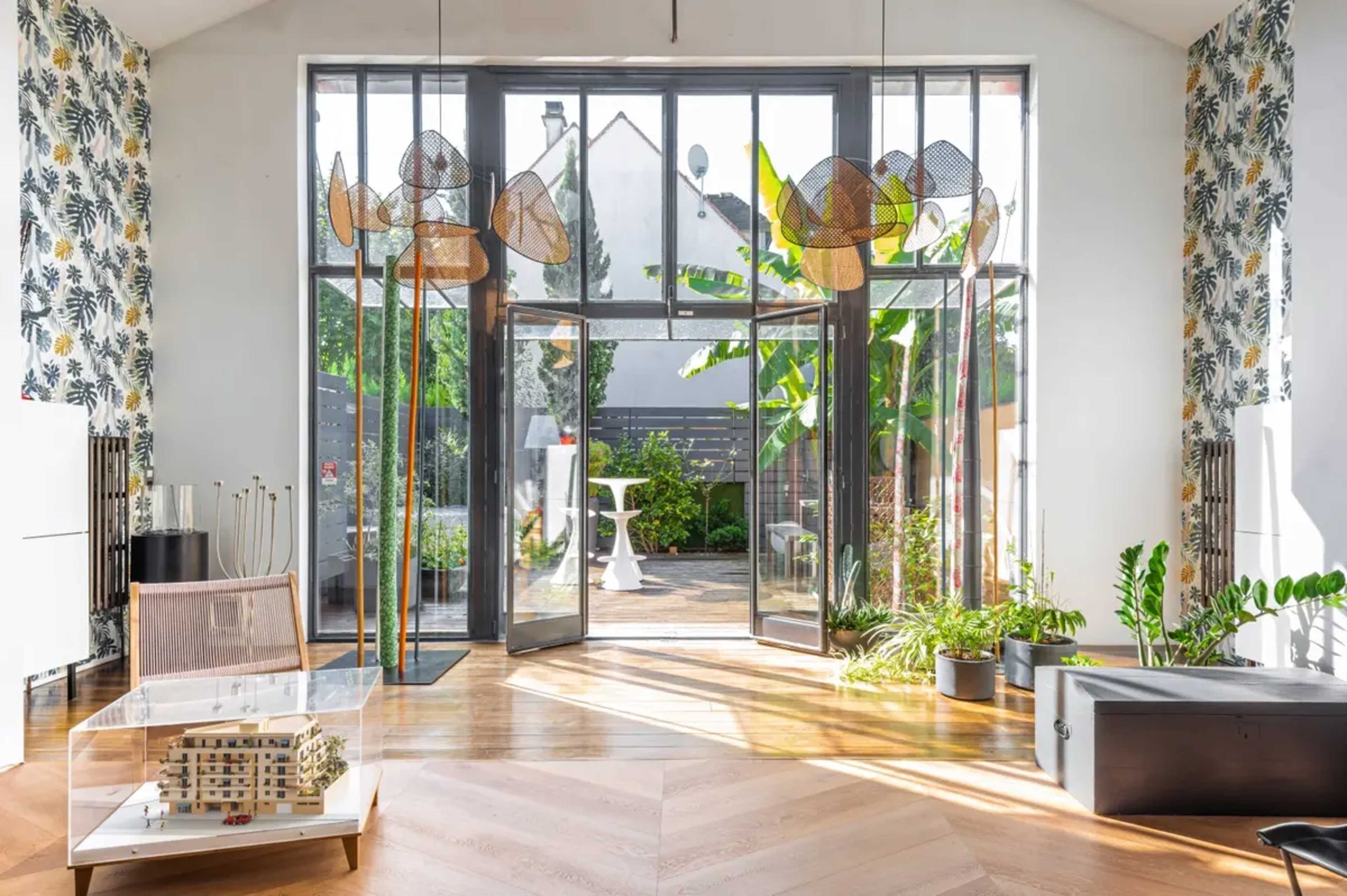 A bright interior space featuring large glass doors that open to a garden, with modern furniture and artistic light fixtures.