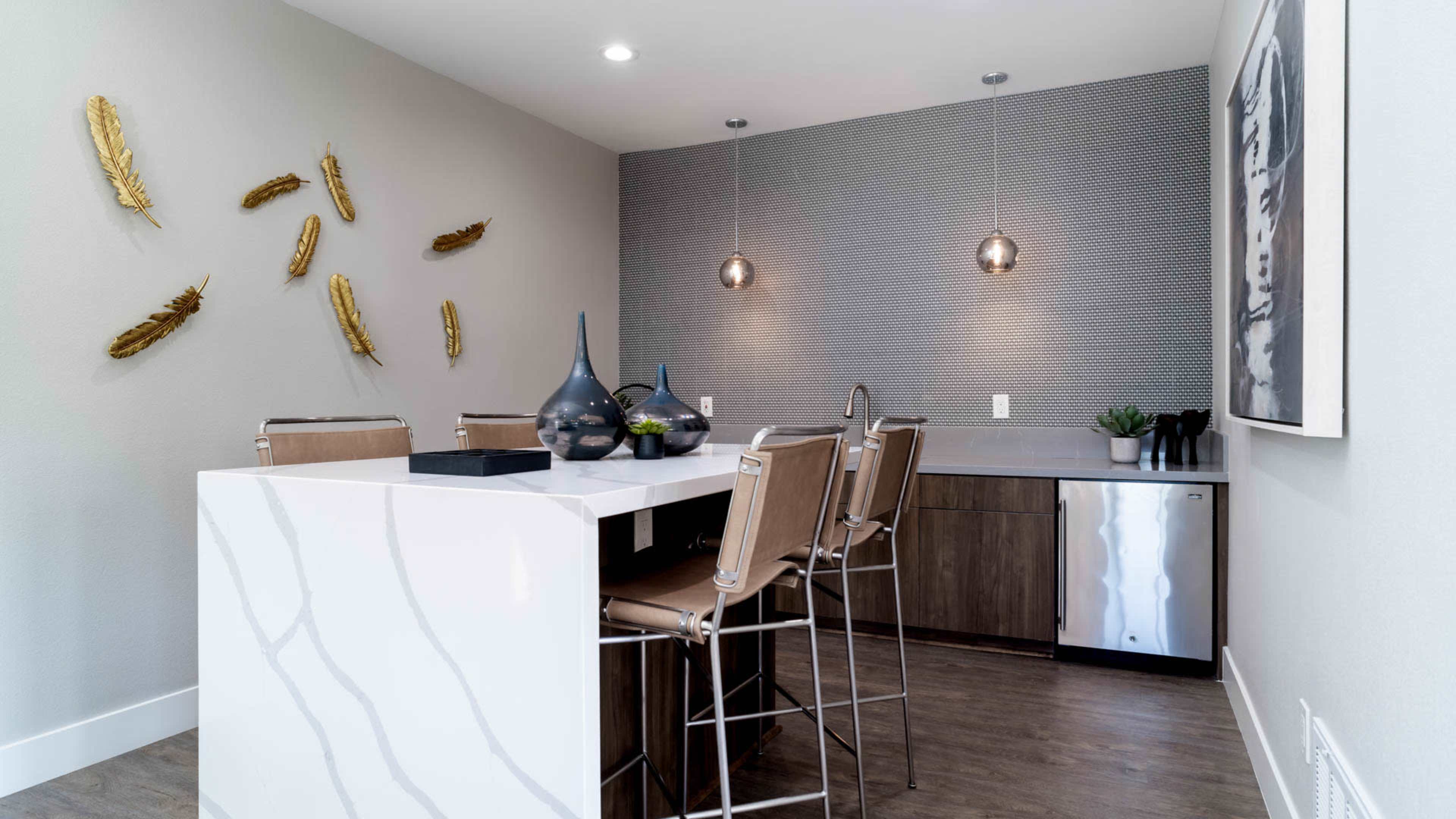 A modern kitchen with a white marble-topped island, bar stools, and decorative wall elements in a neutral color scheme.