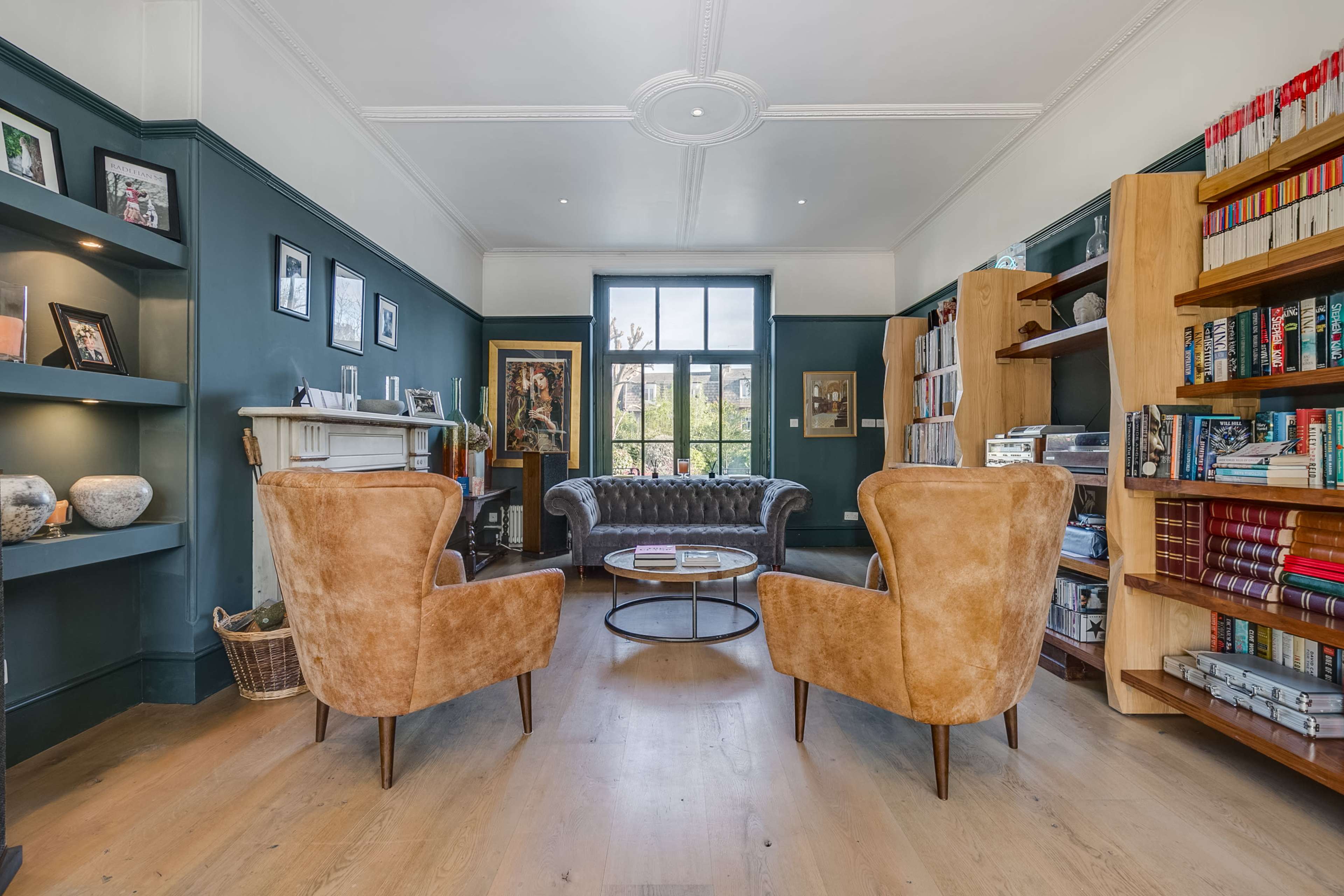 A well-furnished living room featuring two armchairs facing a coffee table, a fireplace, and shelves lined with books and decorative items.