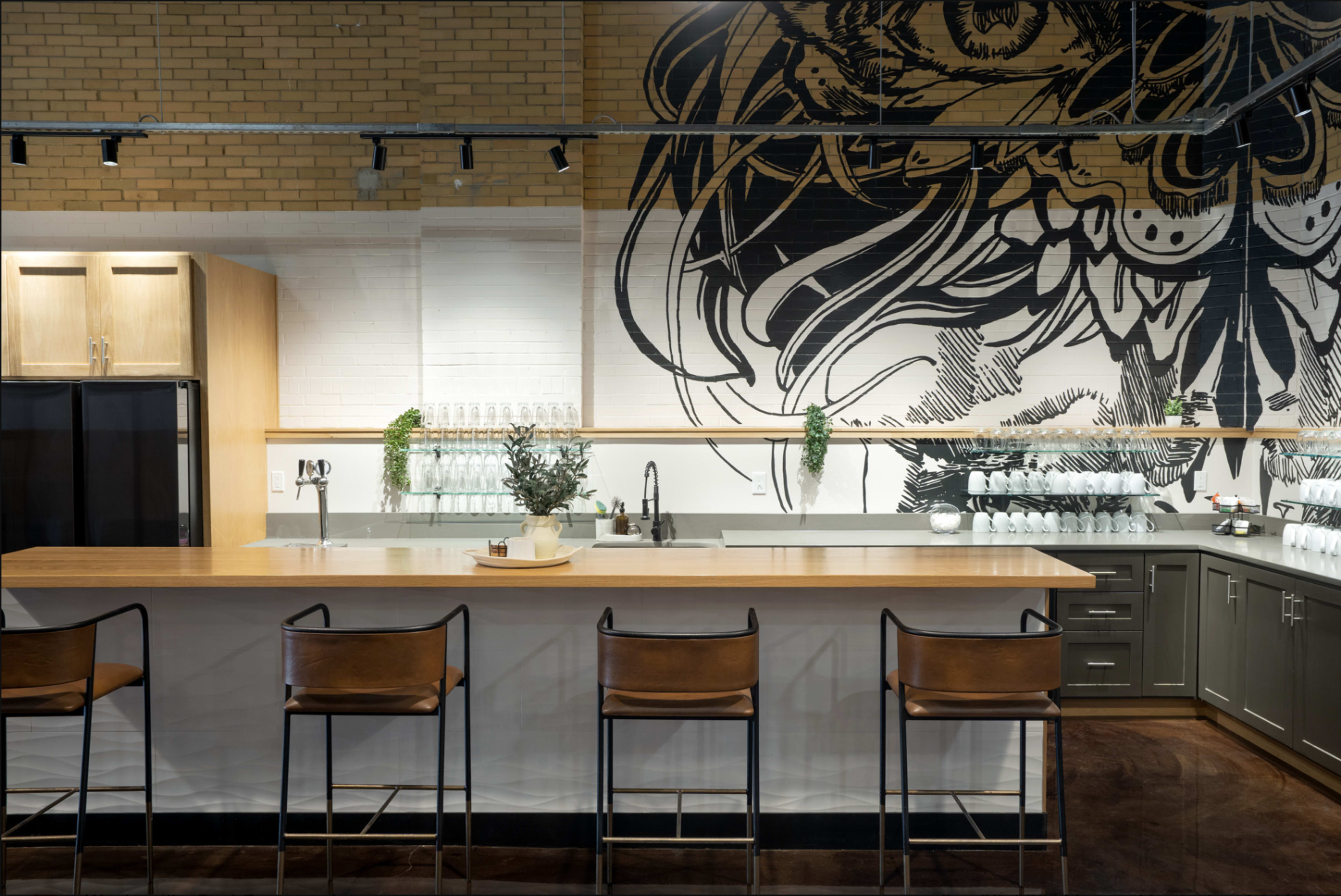 The image shows a modern kitchen with a large island bar featuring high stools and a mural of an abstract design on the wall behind it.