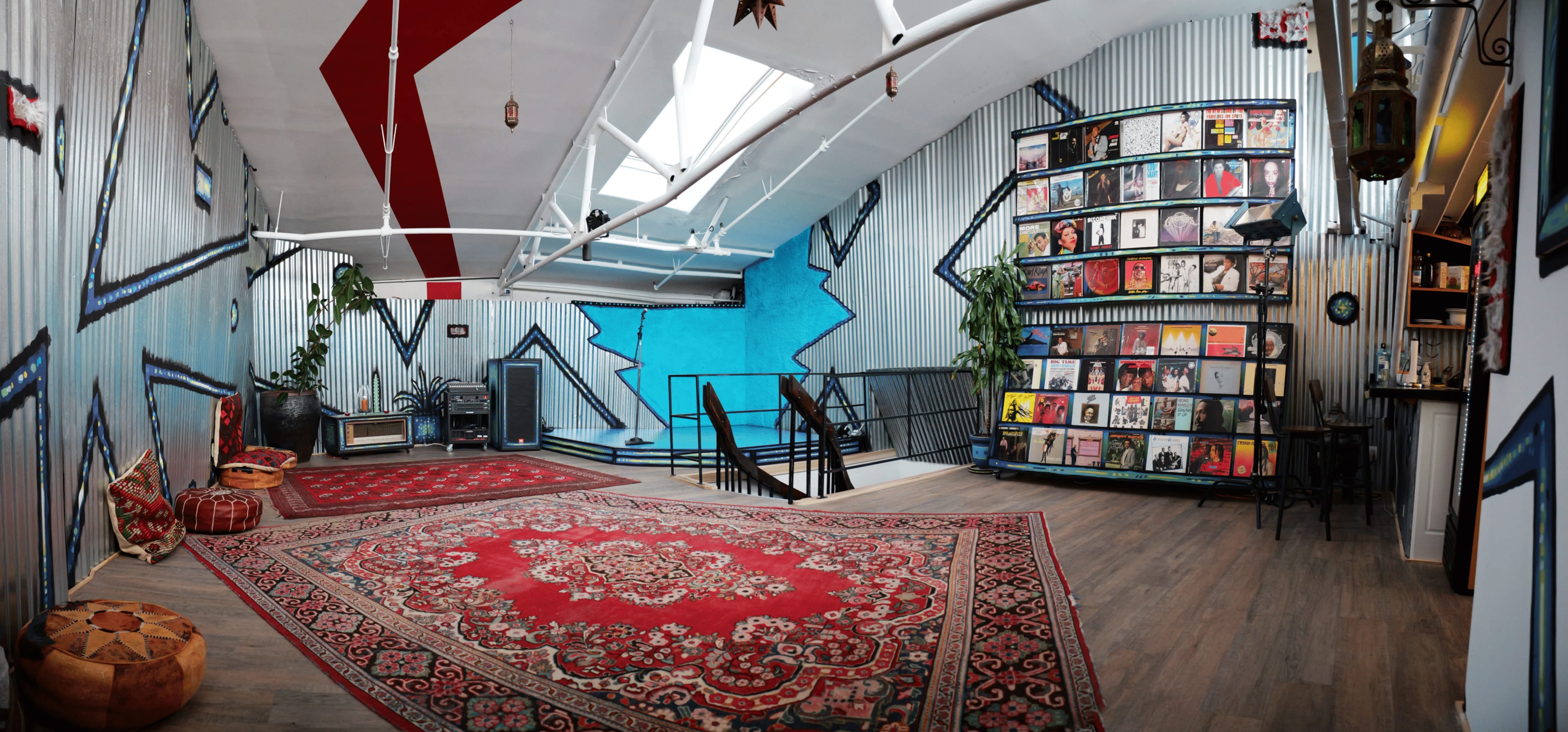 A spacious interior with colorful murals, a patterned rug, and a display of vinyl records on shelves against a blue wall.