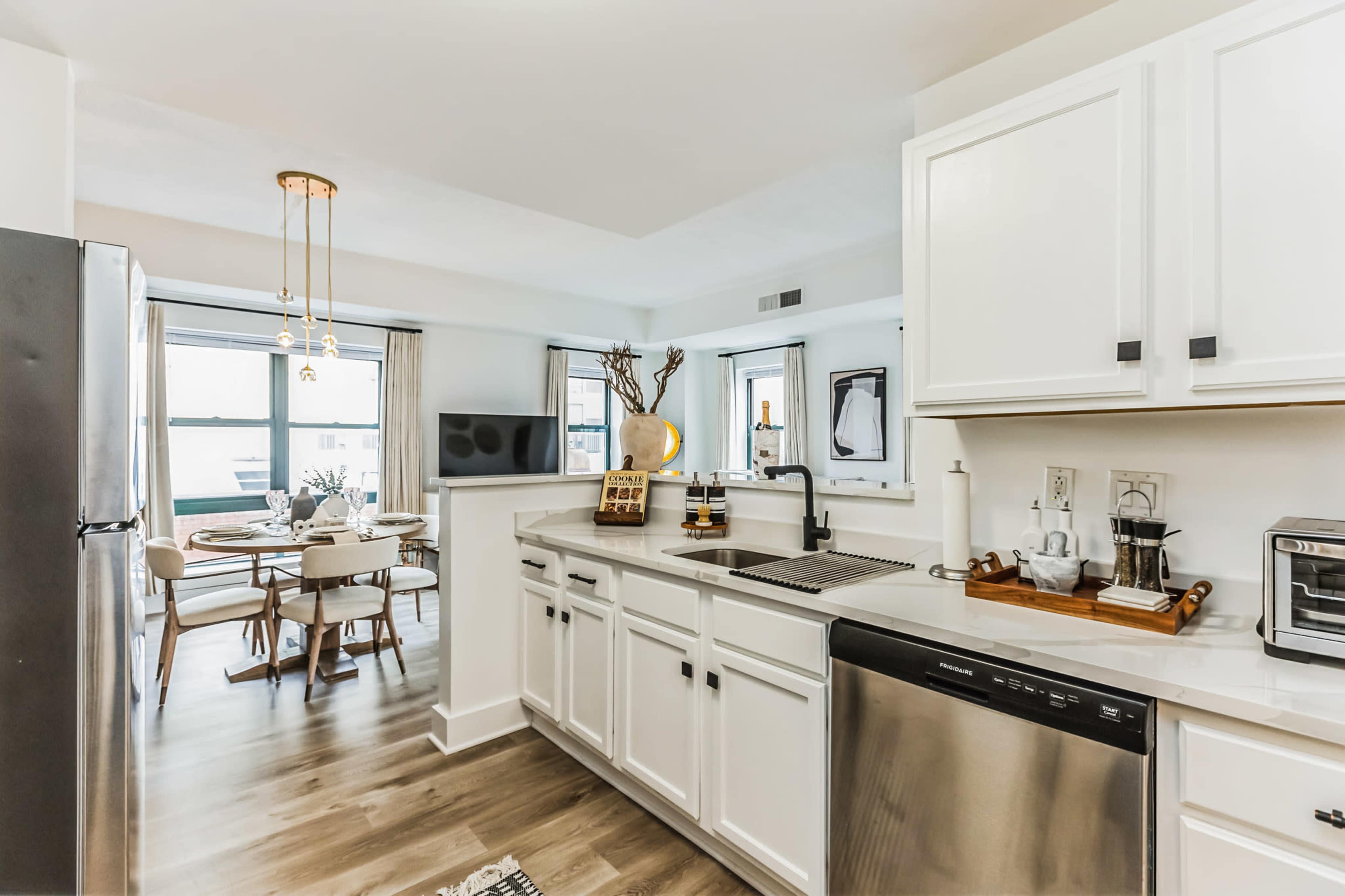 A modern kitchen with white cabinetry, stainless steel appliances, and a dining area featuring a round table and chairs near large windows.