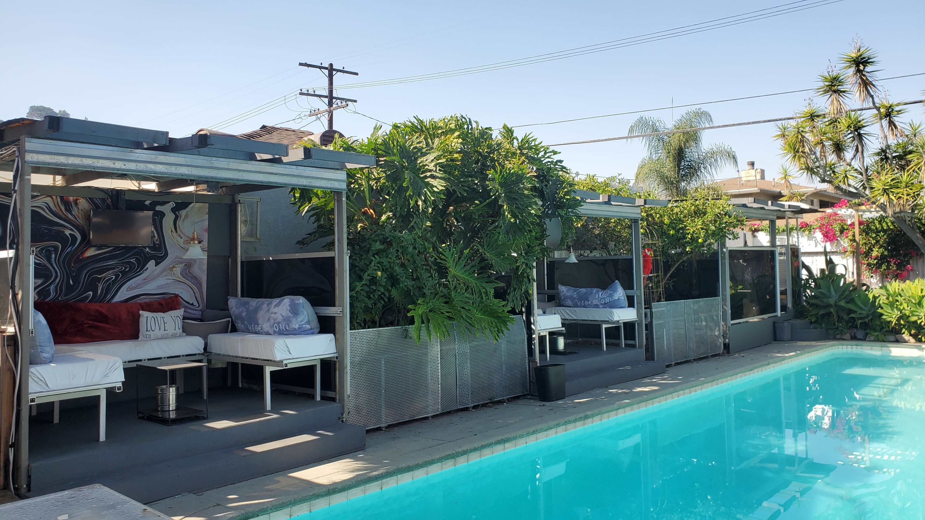 The image shows a swimming pool with several cabanas and lush greenery surrounding the area.
