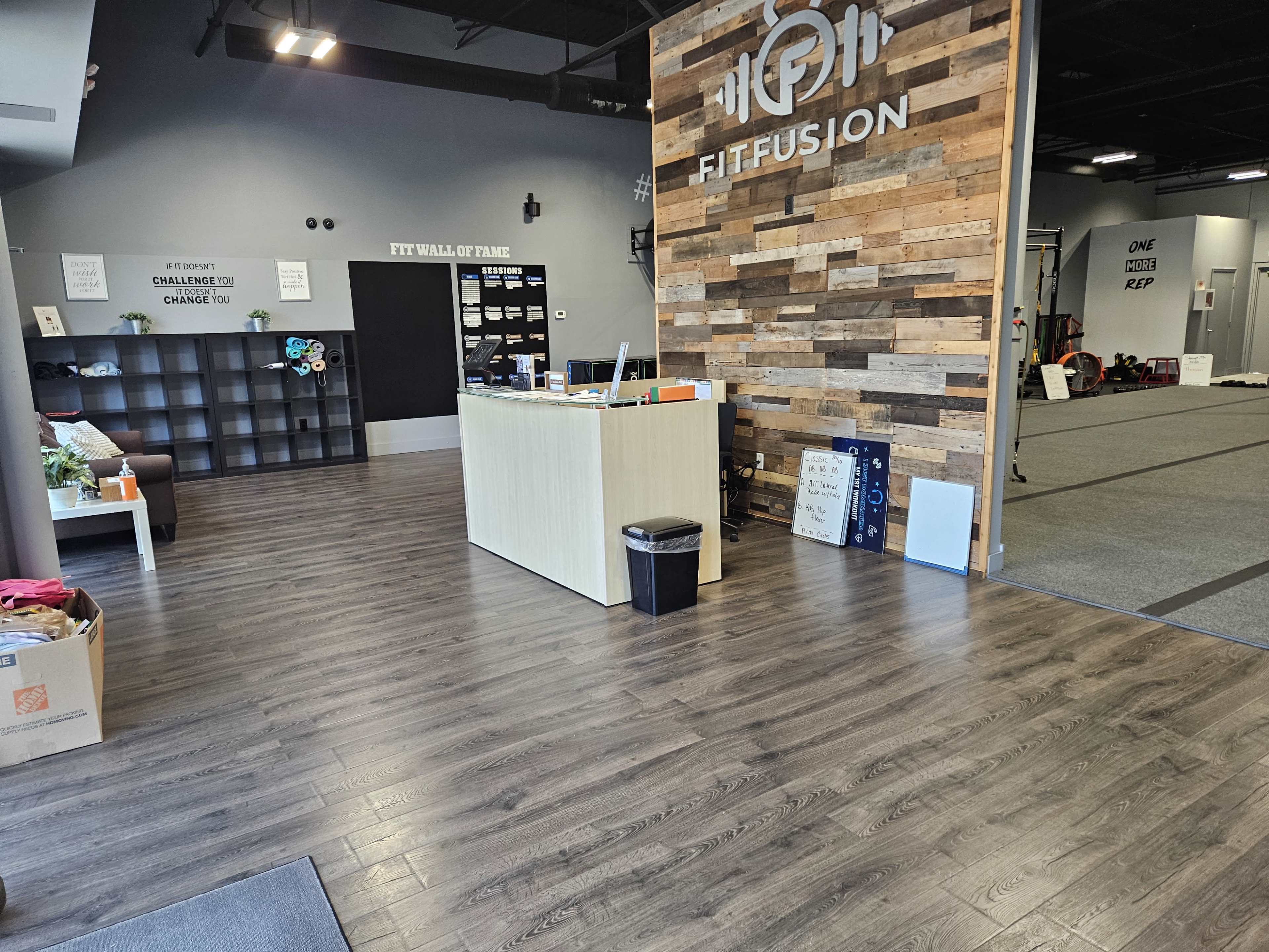 The interior of a fitness center reception area with wooden accent walls, a front desk, and a clean floor.