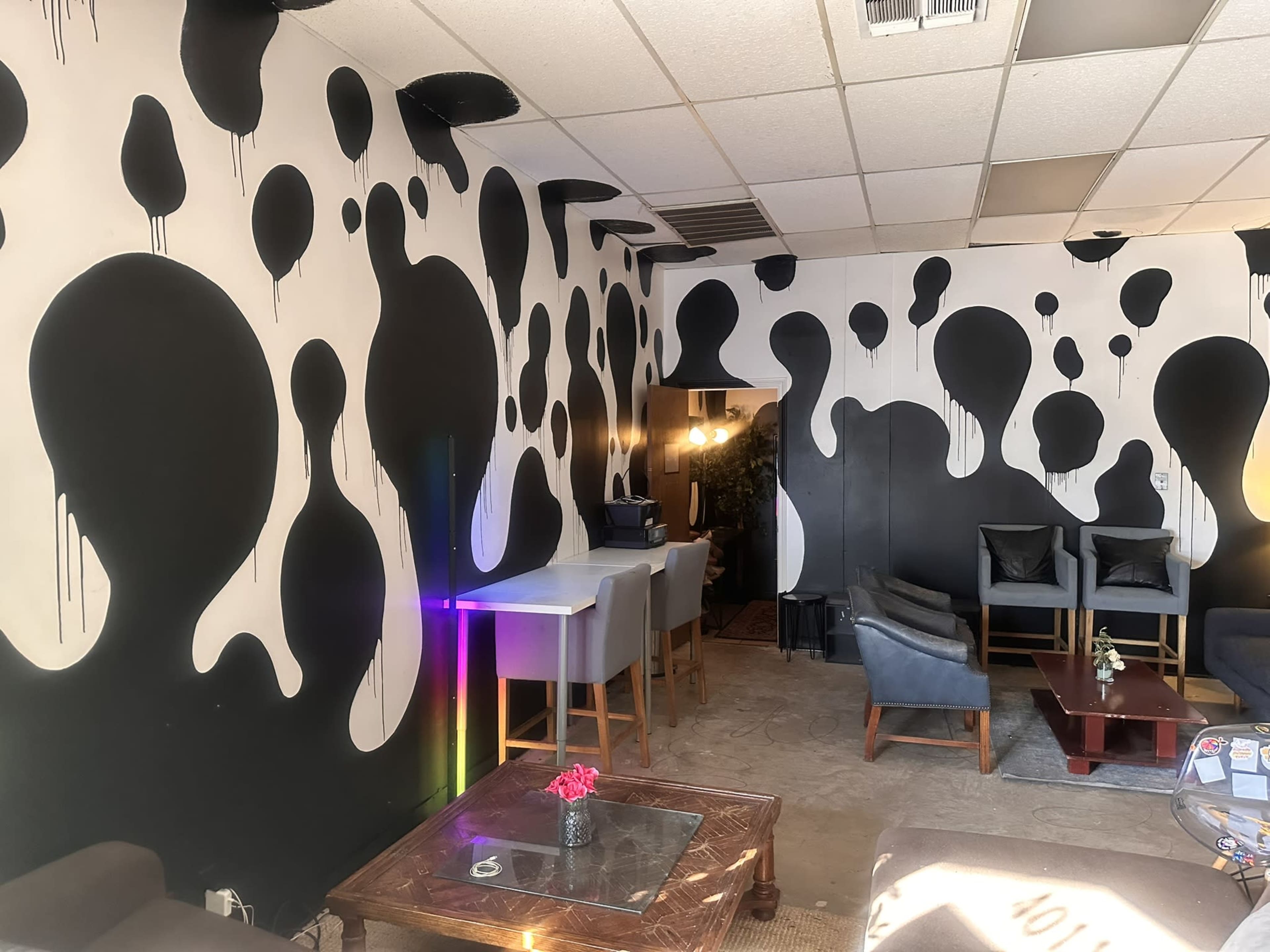 The image depicts a lounge area featuring walls adorned with abstract black and white designs, with seating arrangements including blue chairs and small tables.