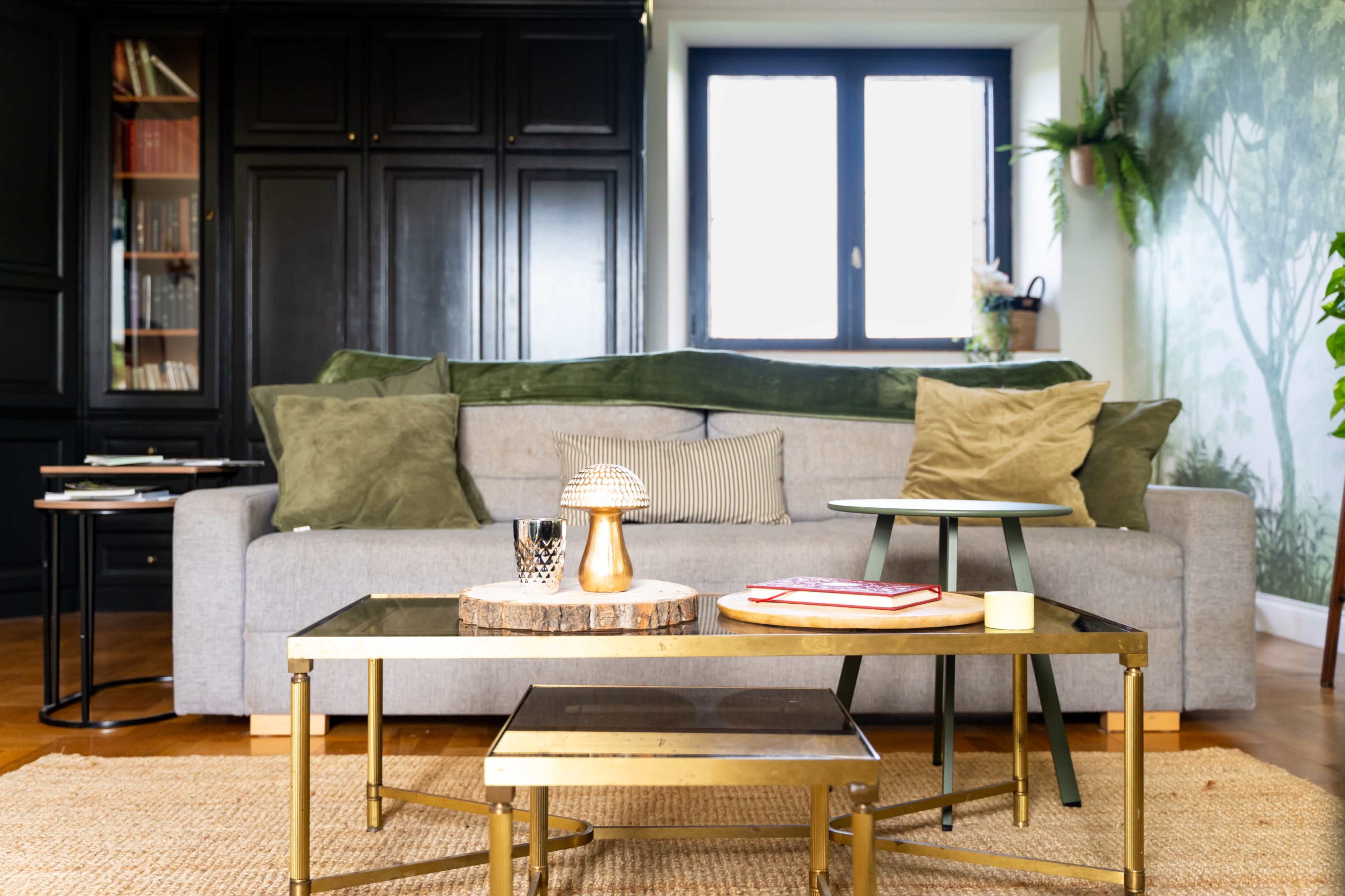 The image shows a stylish living room with a gray sofa, several decorative cushions, and multiple coffee tables arranged in front.