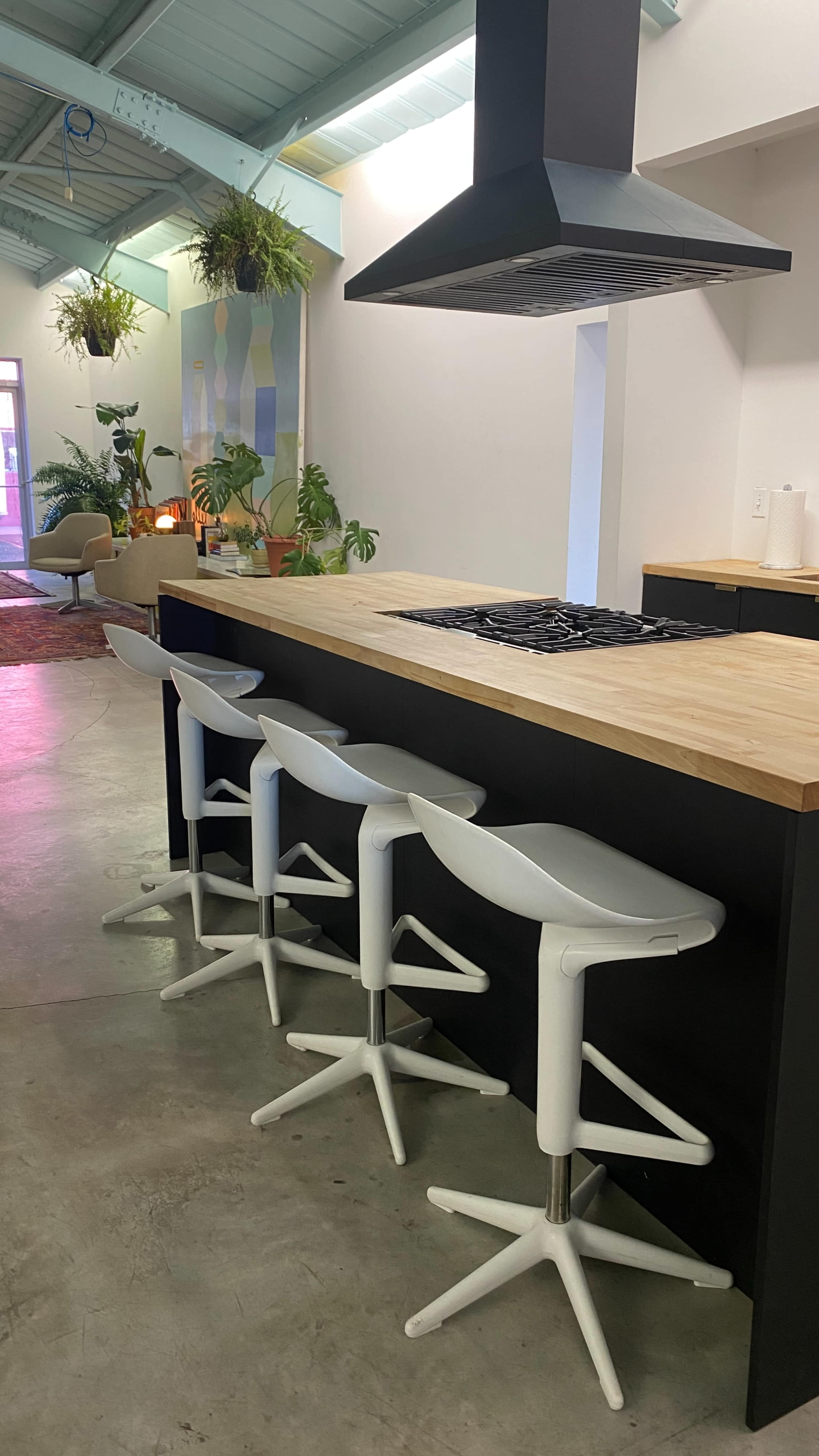 A modern kitchen with a wooden island, a gas cooktop, and four white bar stools.