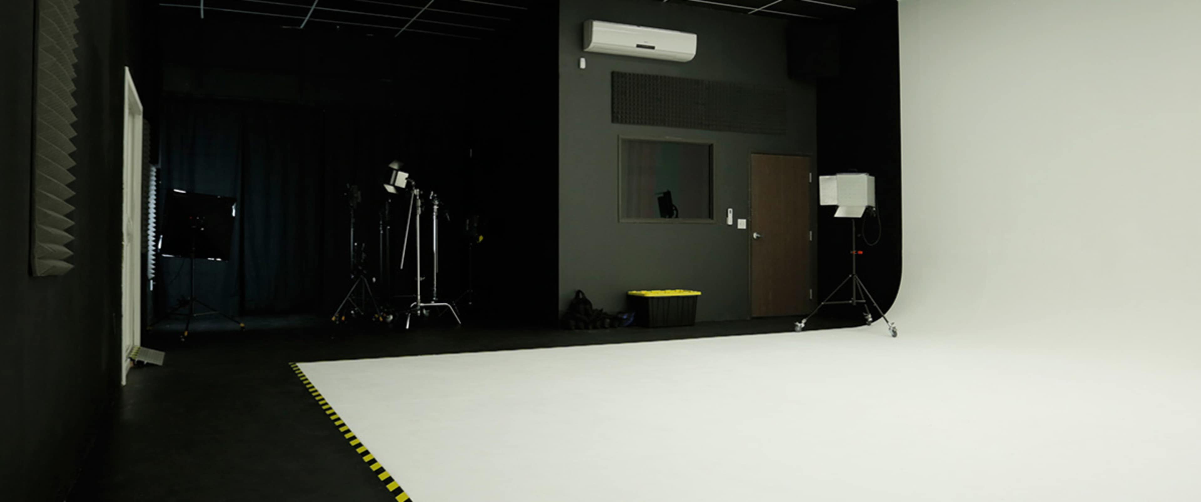 The image shows a photography studio with a white backdrop, lighting equipment, and a dark, minimalistic interior.