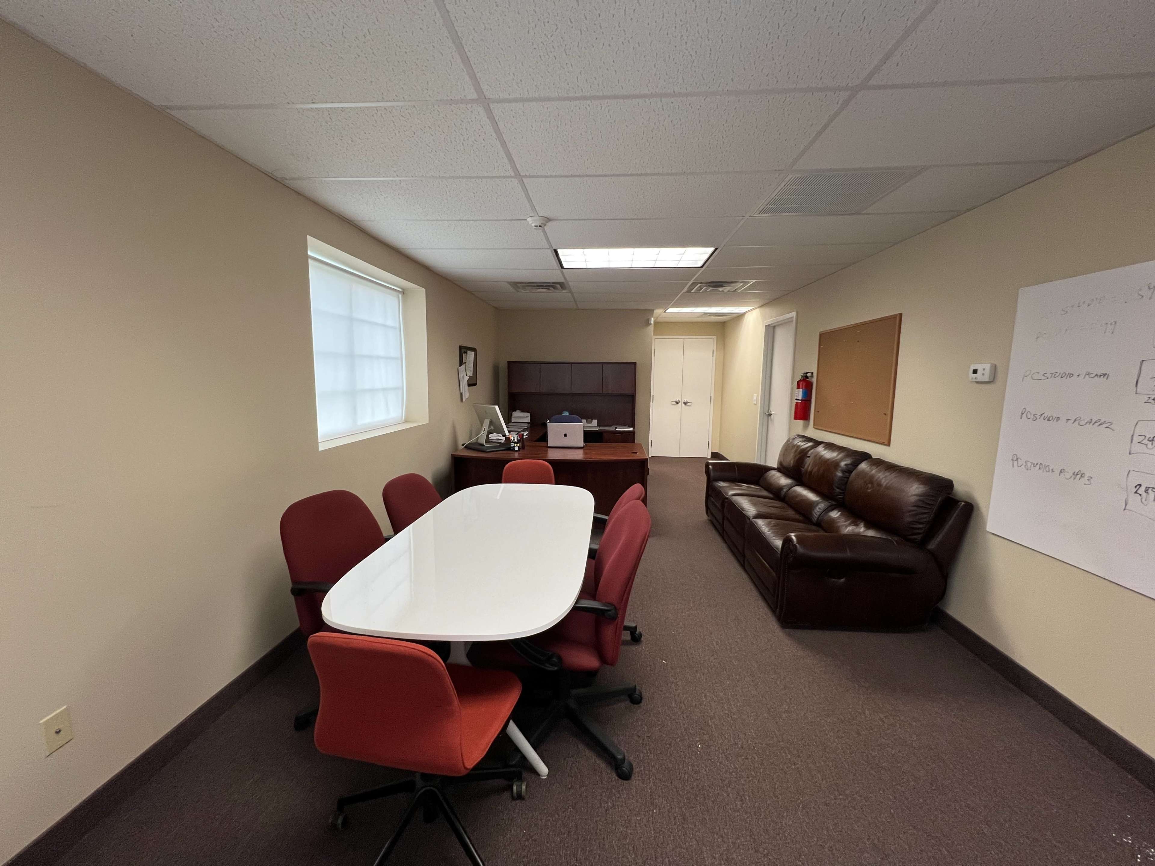 A small office space with a conference table surrounded by red chairs, a brown leather couch, and a desk against the wall.