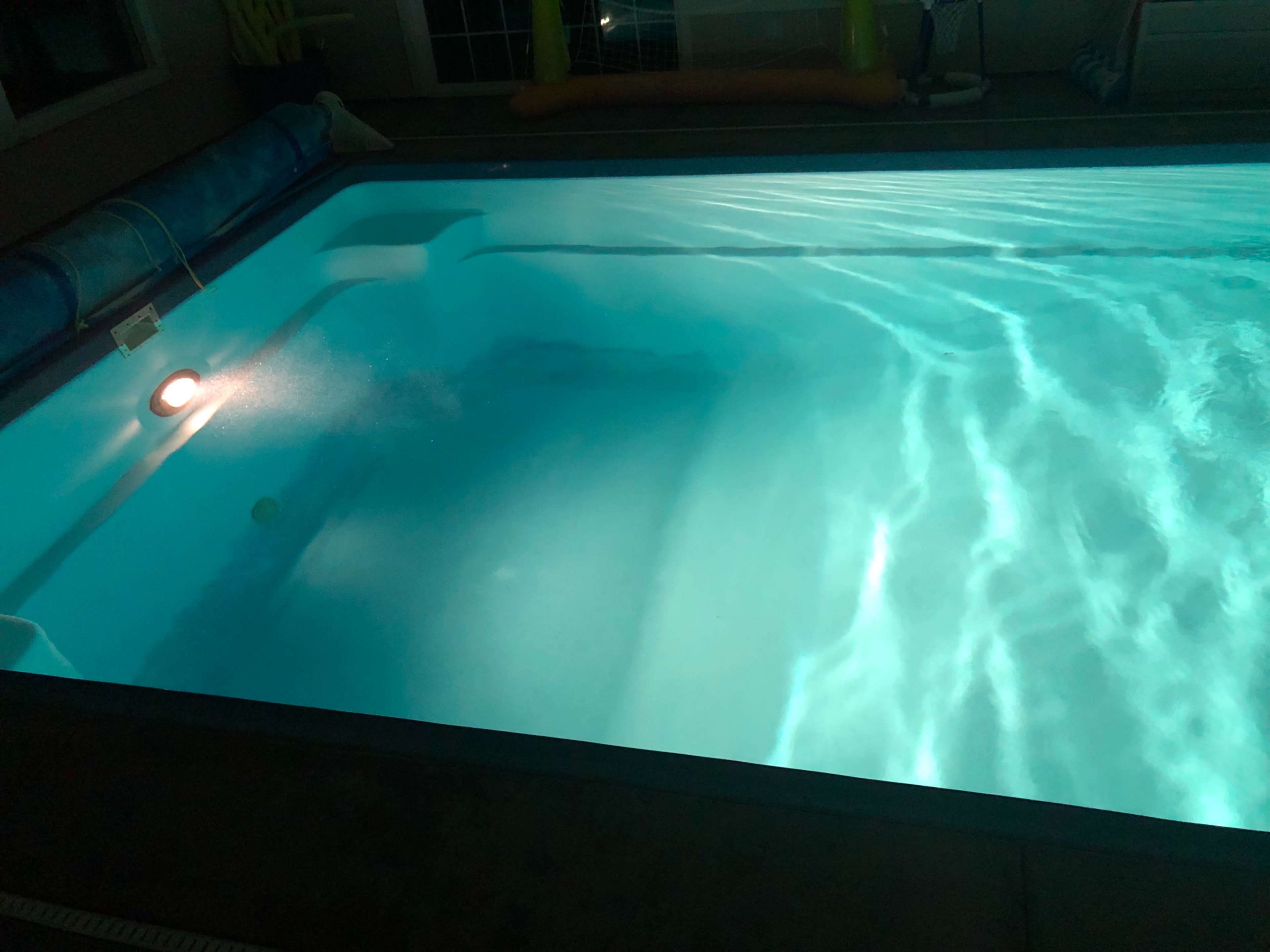 A swimming pool illuminated by underwater lights, reflecting ripples on the surface.