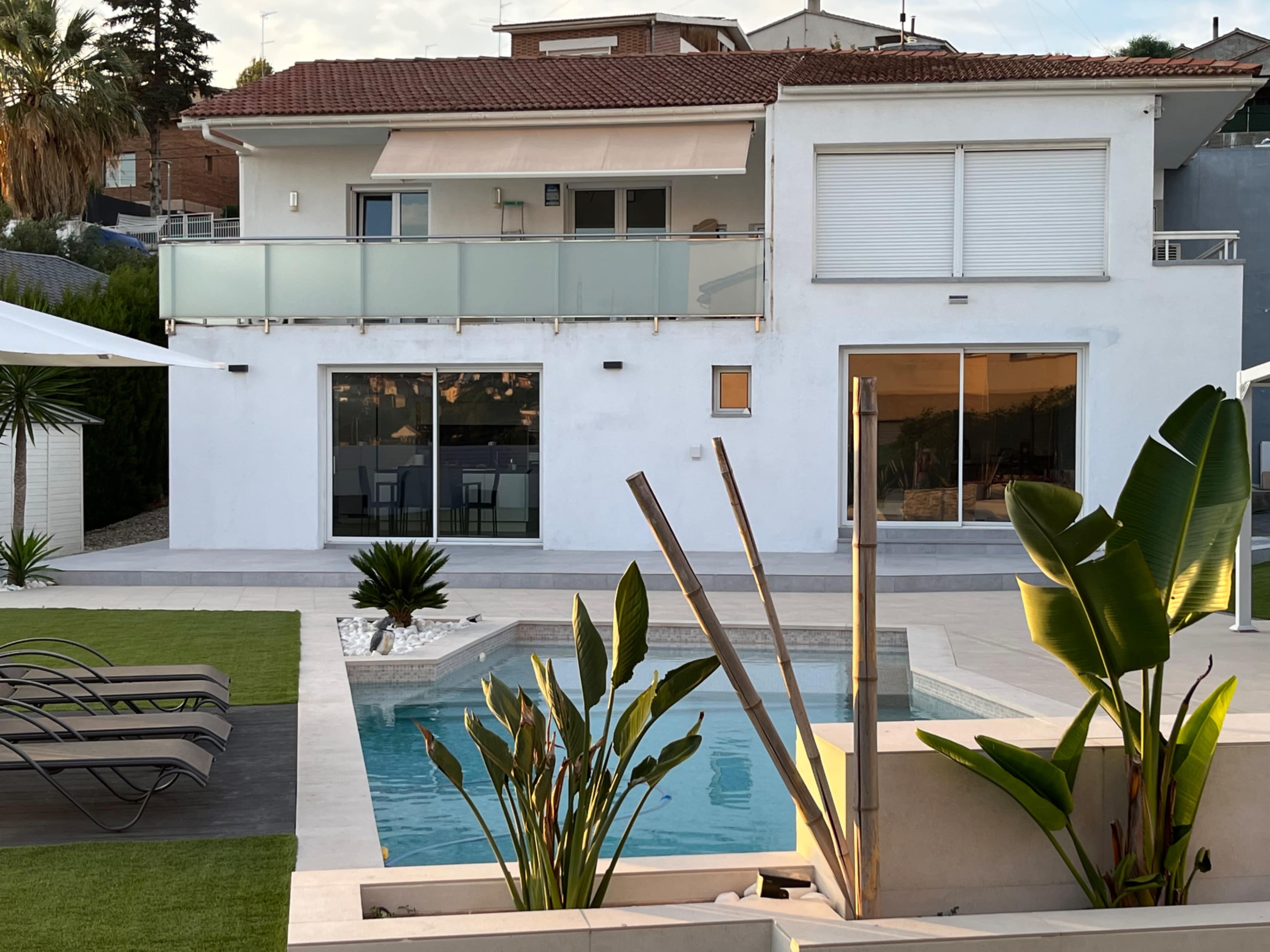 A modern two-story house with a swimming pool, a patio area, and landscaped greenery.