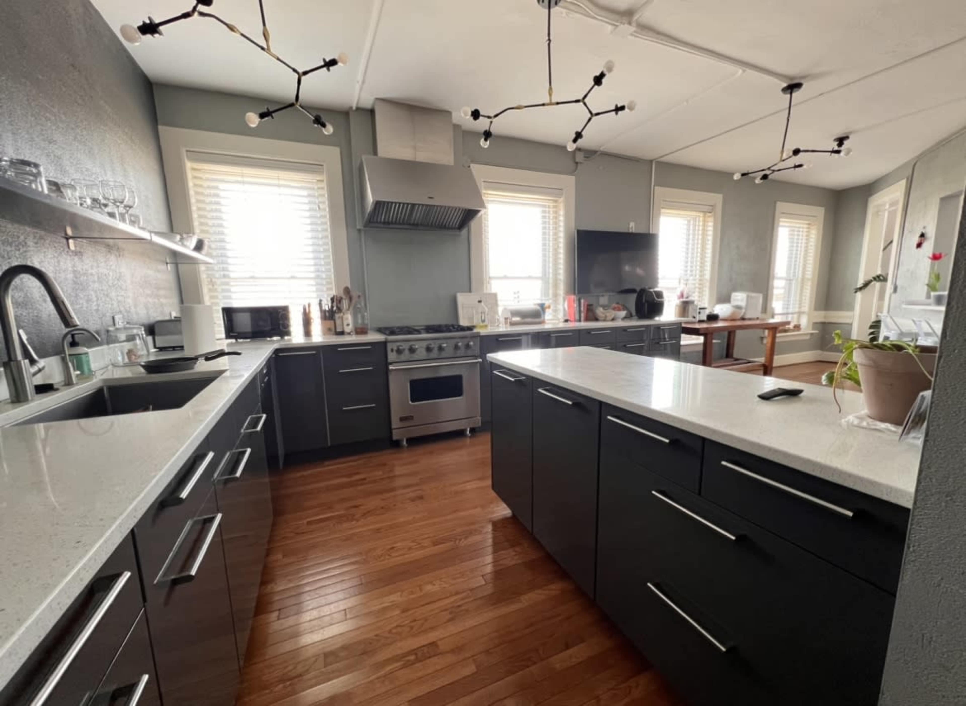 A modern kitchen features dark cabinetry, stainless steel appliances, and a central island with a white countertop, illuminated by unique light fixtures.