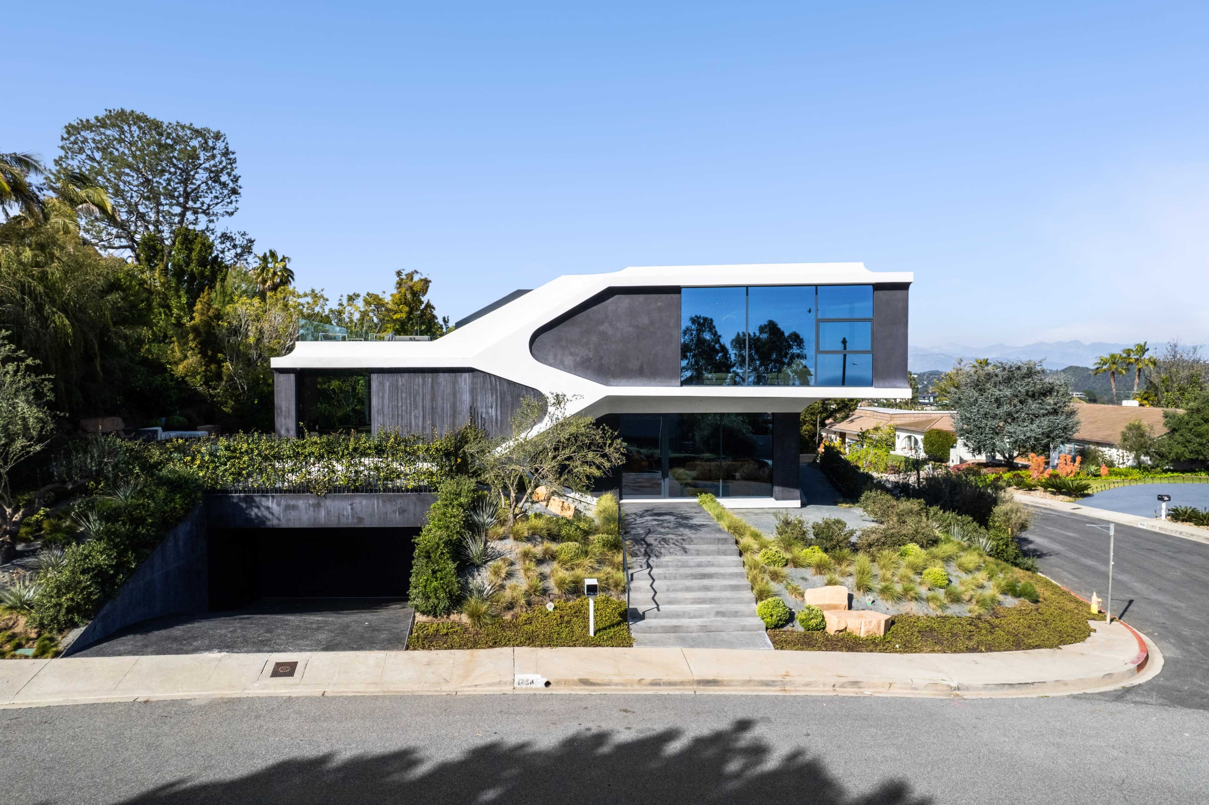 A modern, angular house with large windows and landscaped gardens, situated on a corner lot.