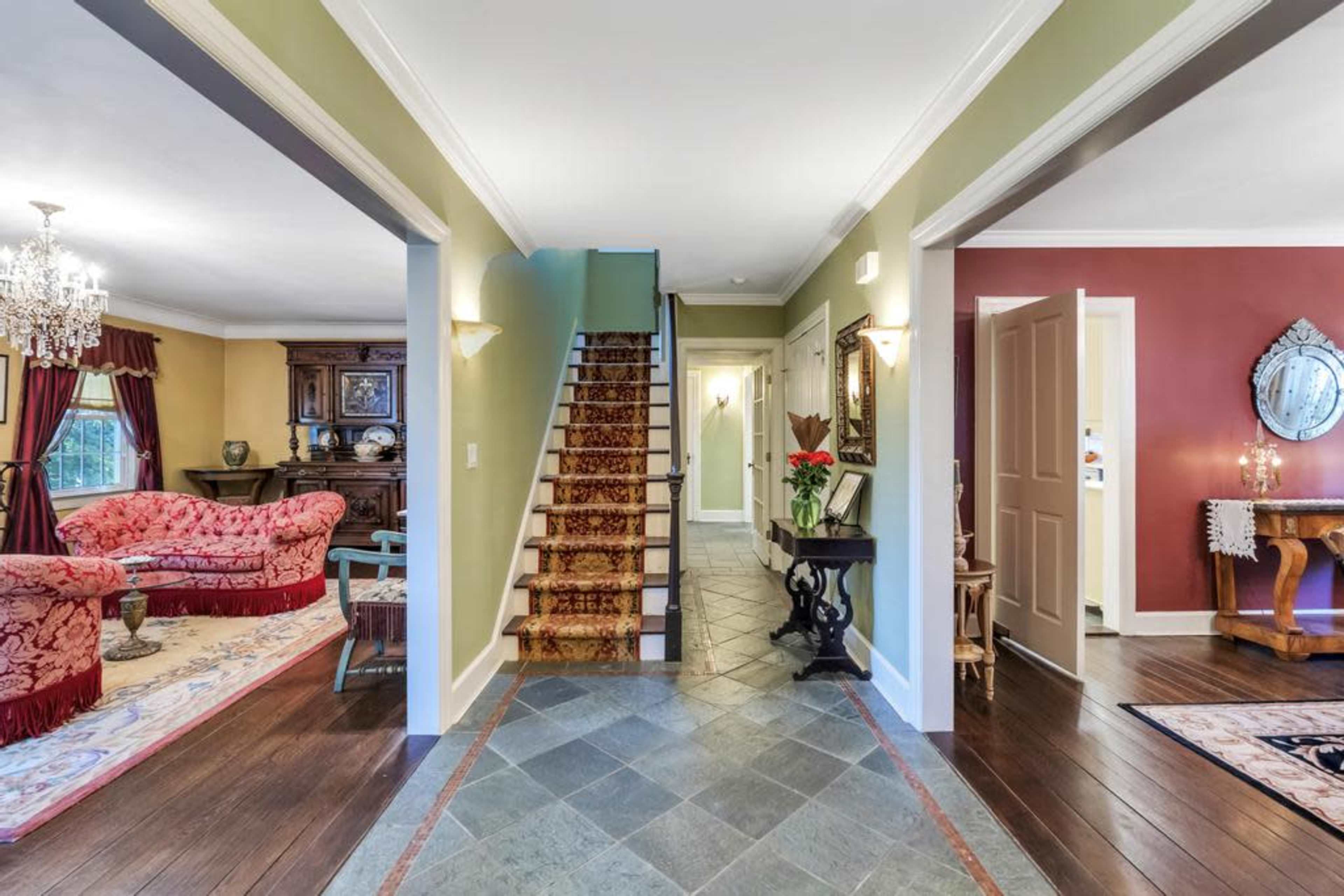 A foyer with a staircase in the center, flanked by a living room to the left and a dining area to the right, featuring various furnishings and decor.