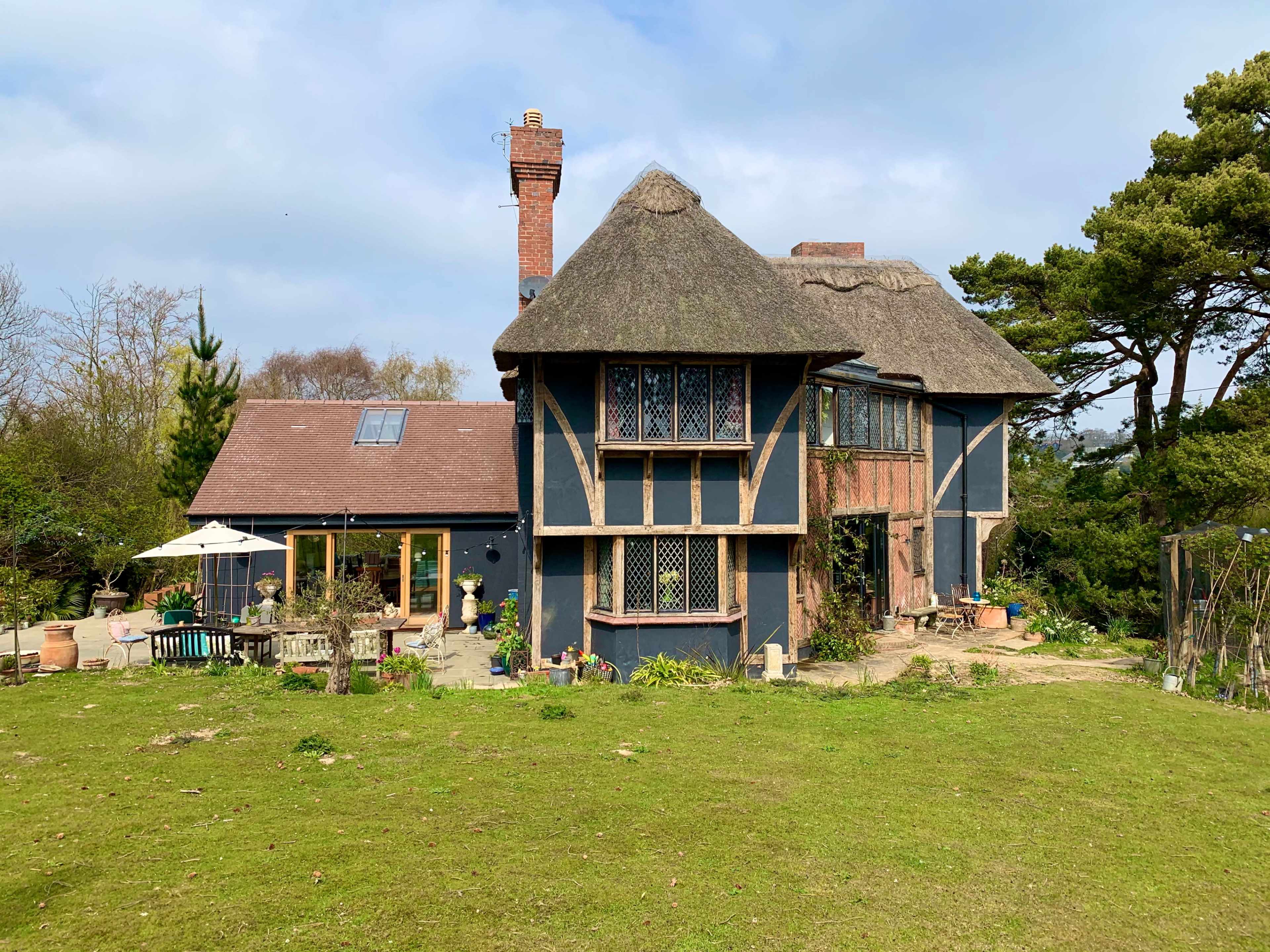 A large, thatched-roof house with a mix of traditional and modern architectural elements, surrounded by greenery.