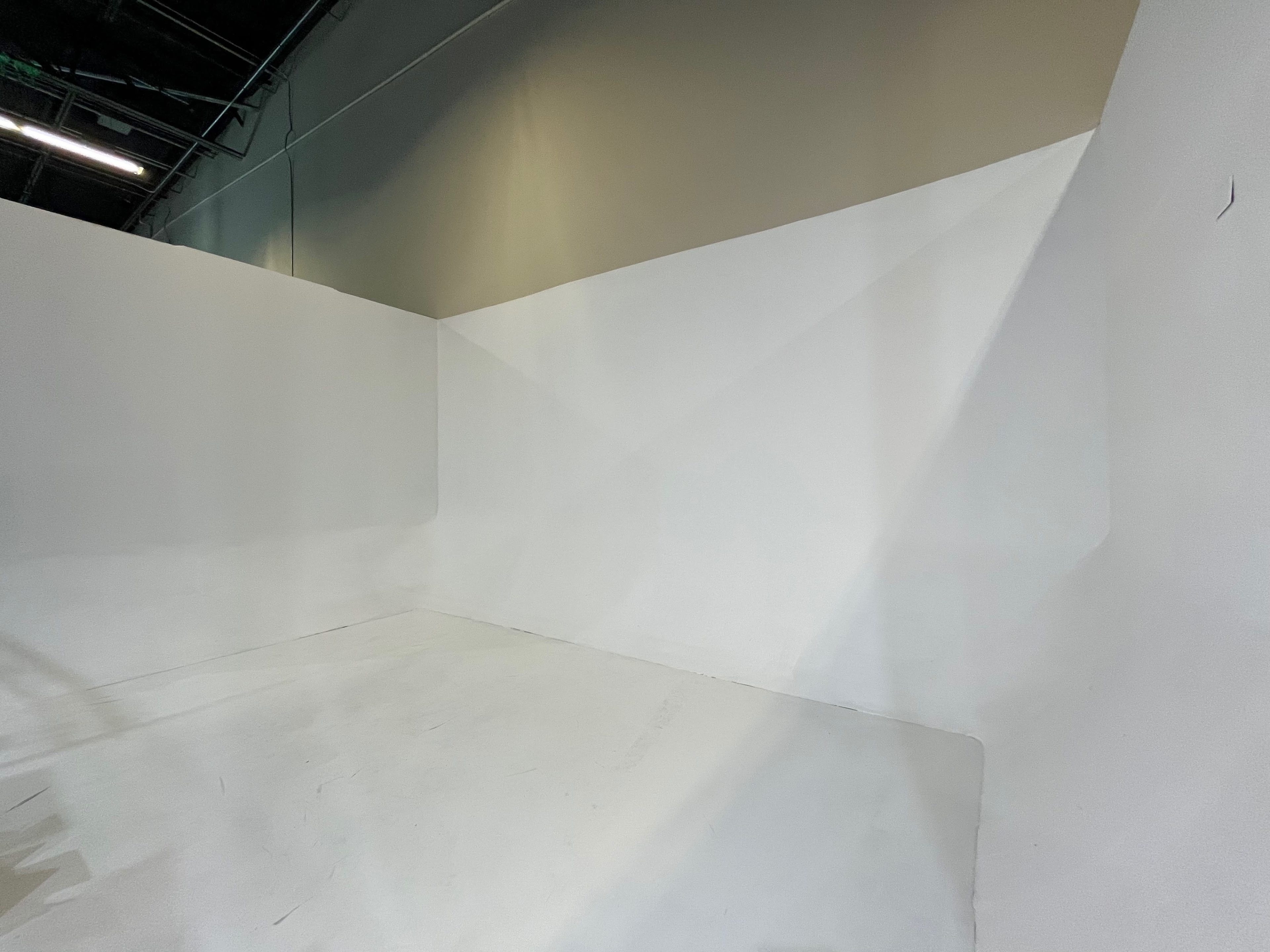 A minimalist white studio space with a slanted wall and a flat floor.