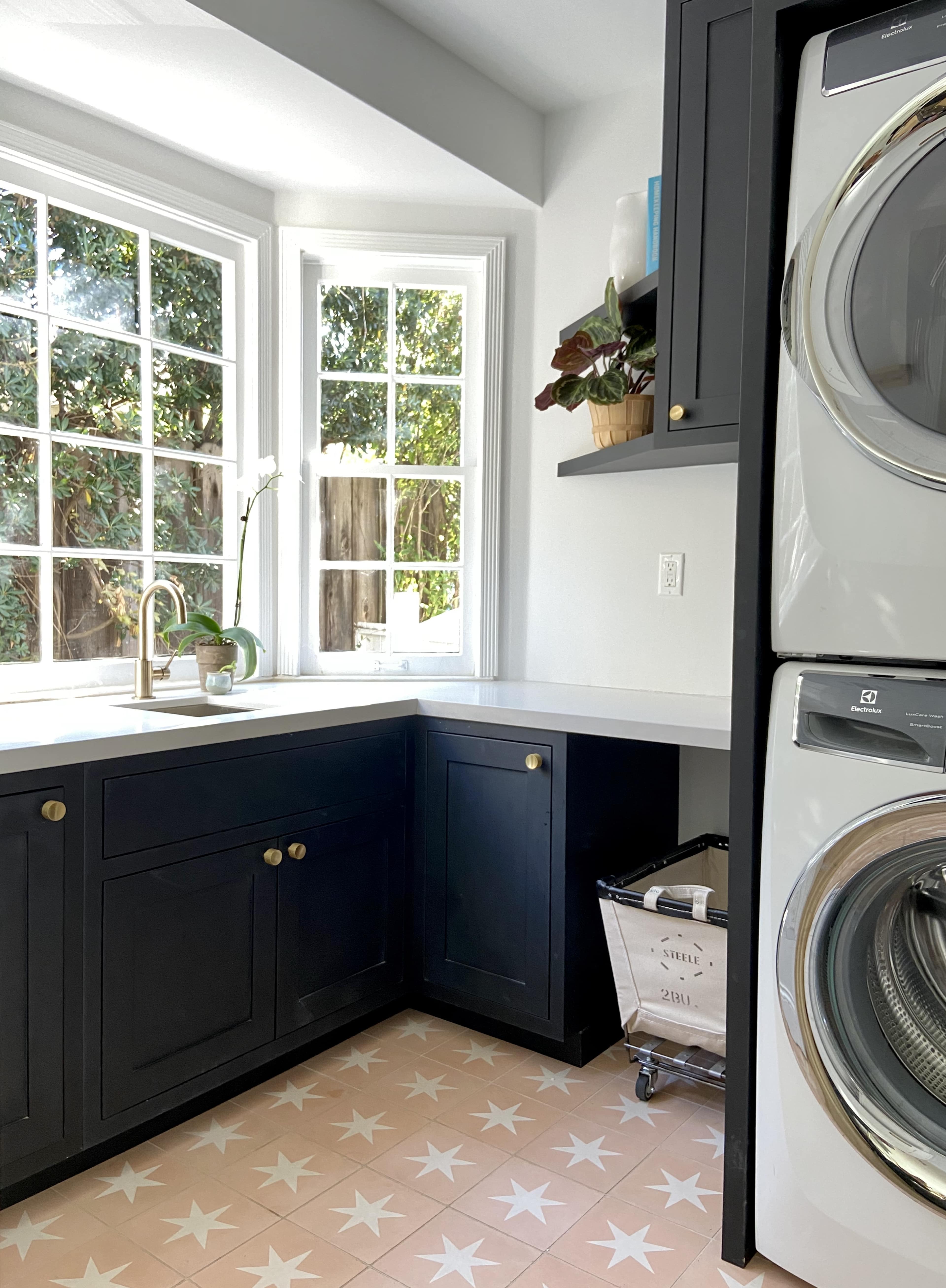 A laundry room features stacked washing machines and a countertop with a sink, illuminated by natural light from windows.