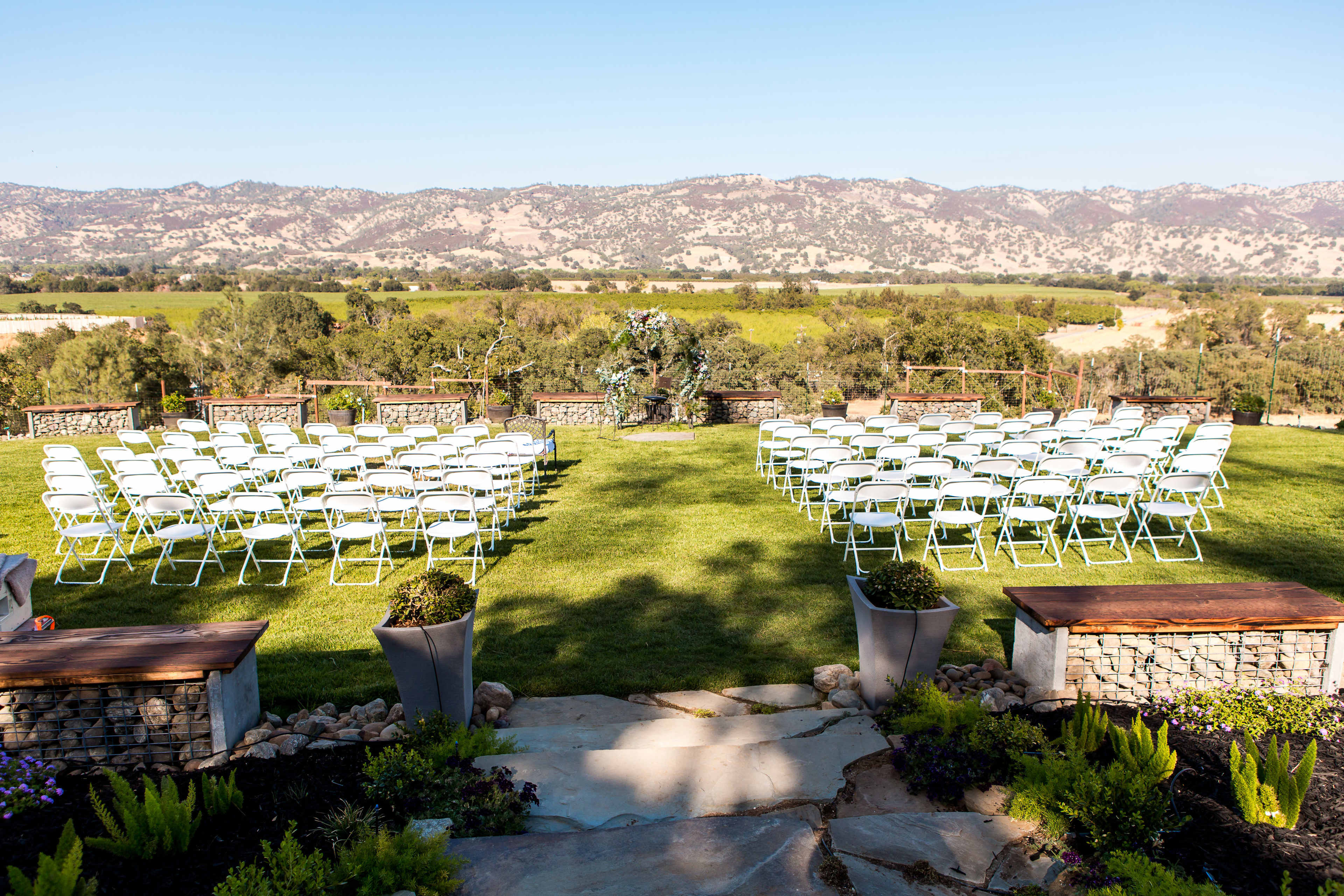 A wedding ceremony setup with rows of white chairs arranged on a grassy lawn overlooking a mountainous landscape.