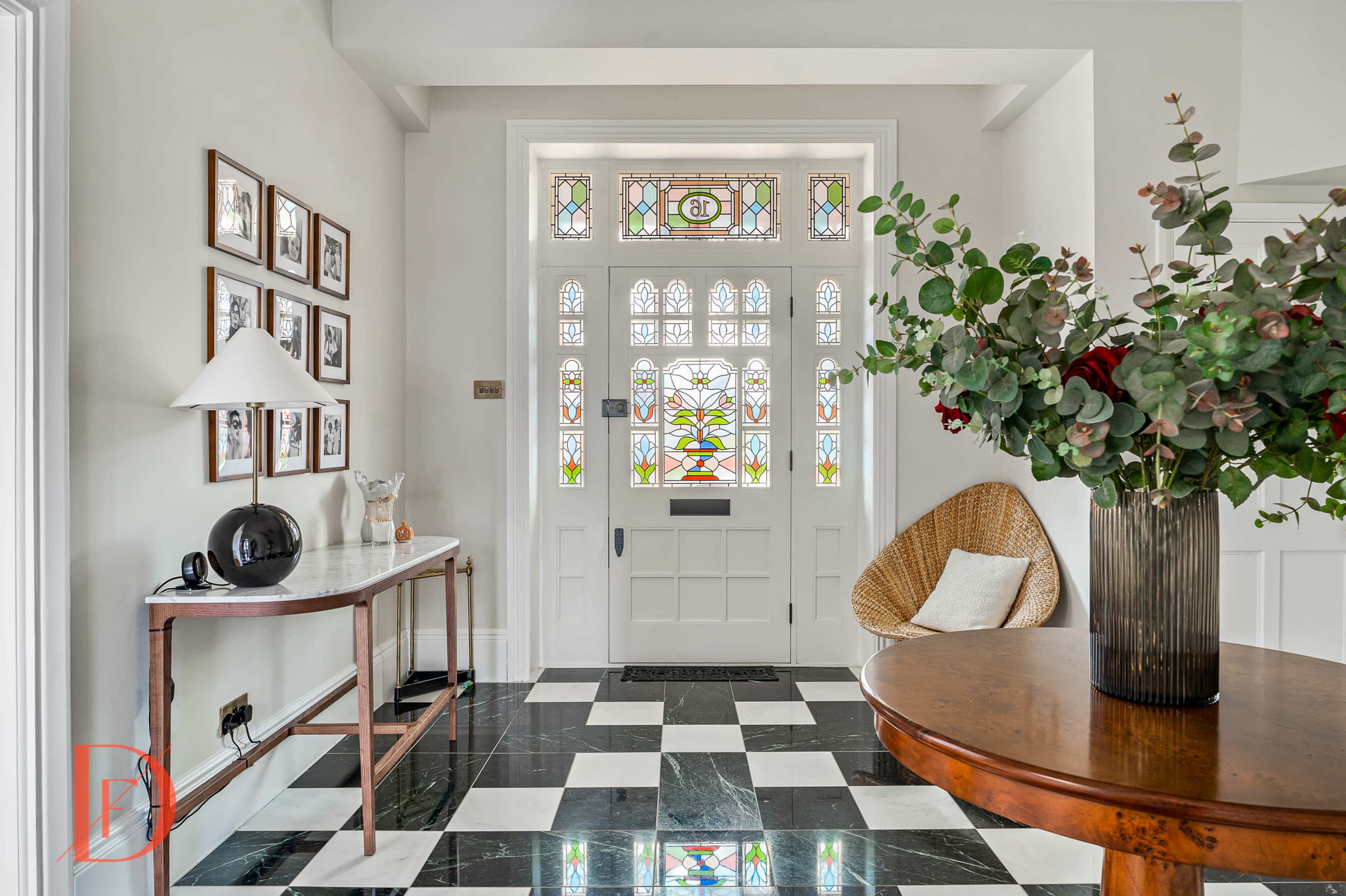 An entryway with a checkerboard black and white floor, a stained glass door, and a table adorned with a vase of flowers and decorative items.