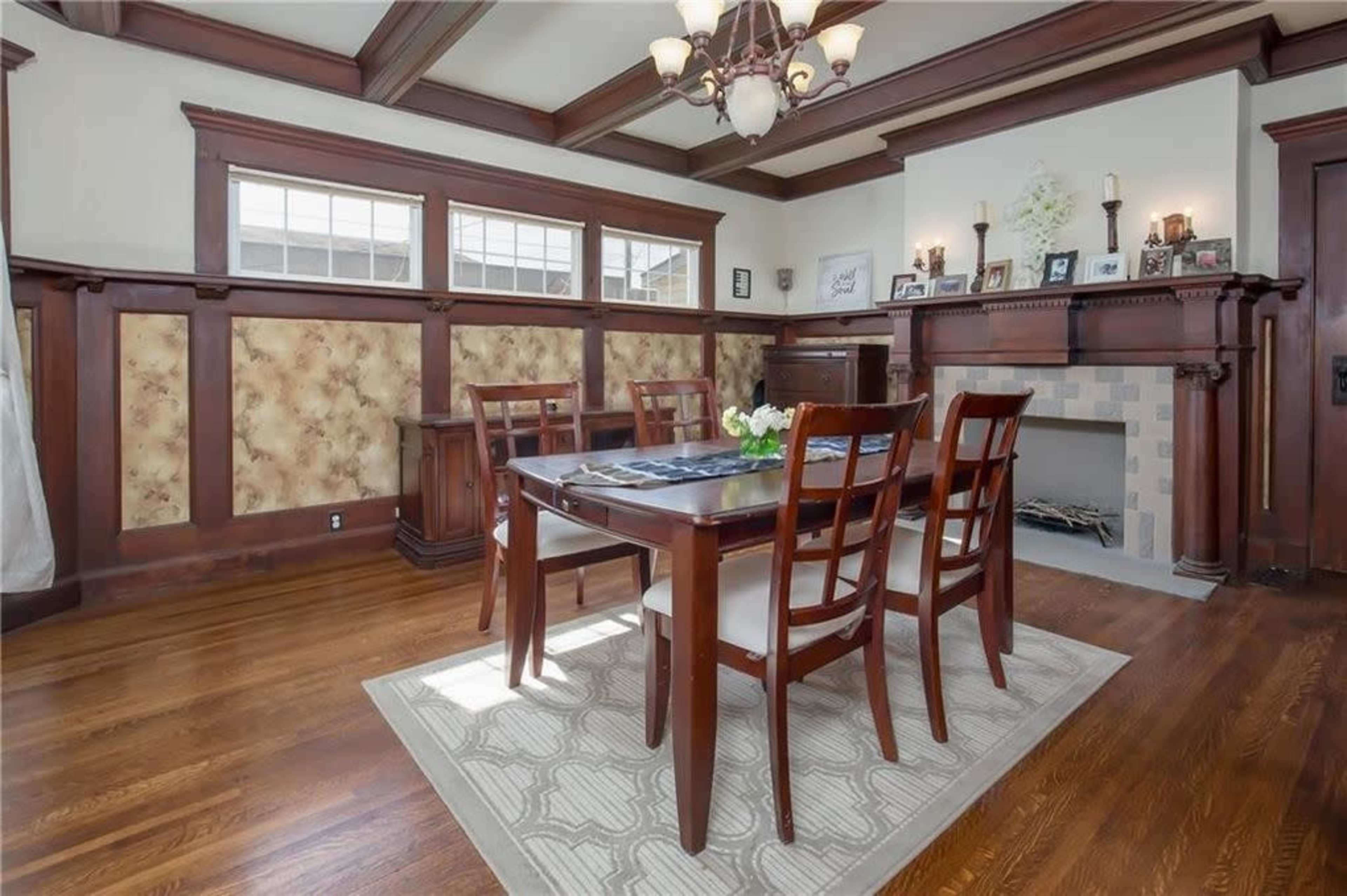 A dining room features a wooden table surrounded by chairs, with a fireplace and paneled walls adorned with decorative accents.