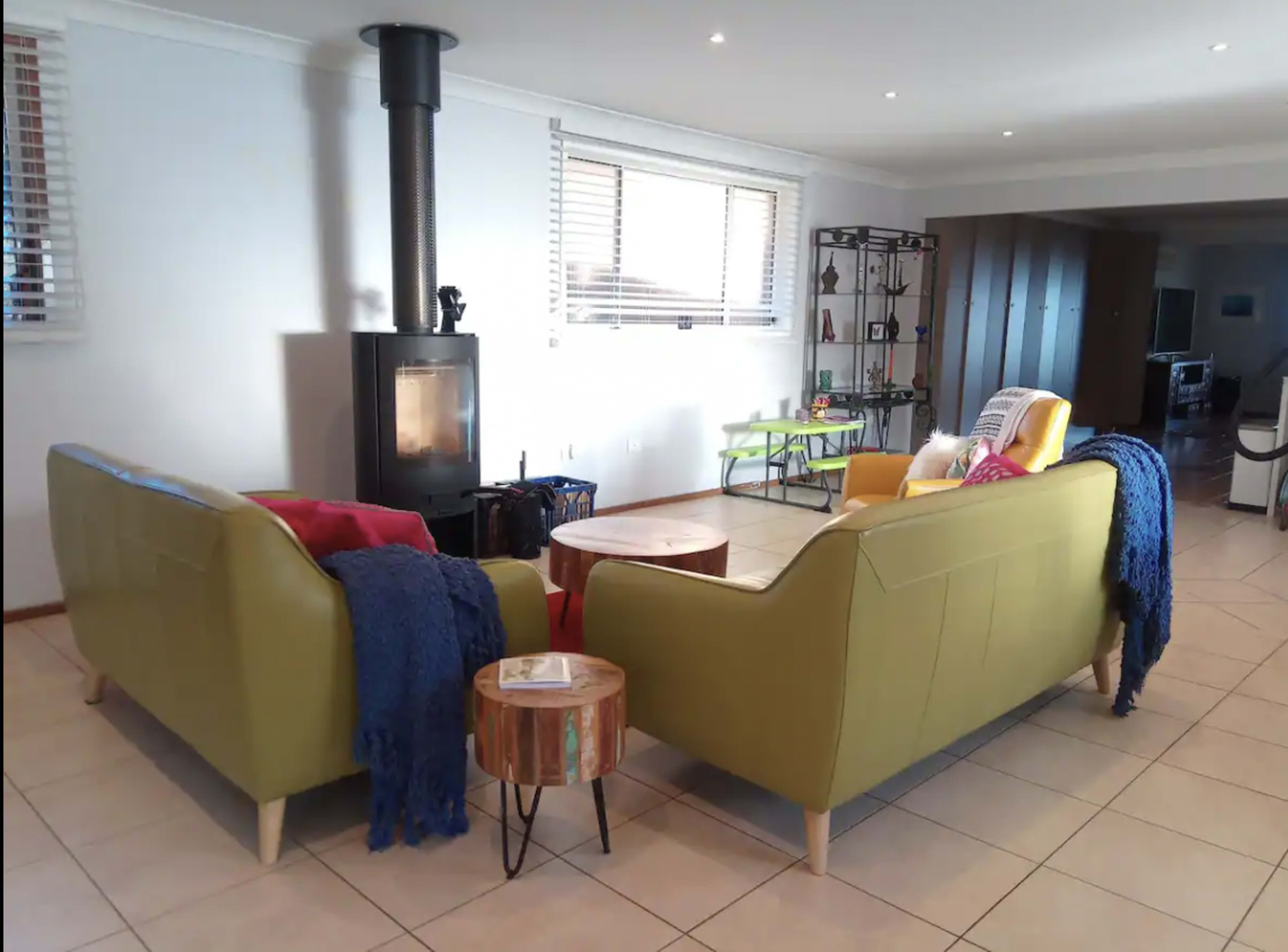 A cozy living room features two sofas facing each other, a wood-burning stove, and a small round table surrounded by various seating arrangements.